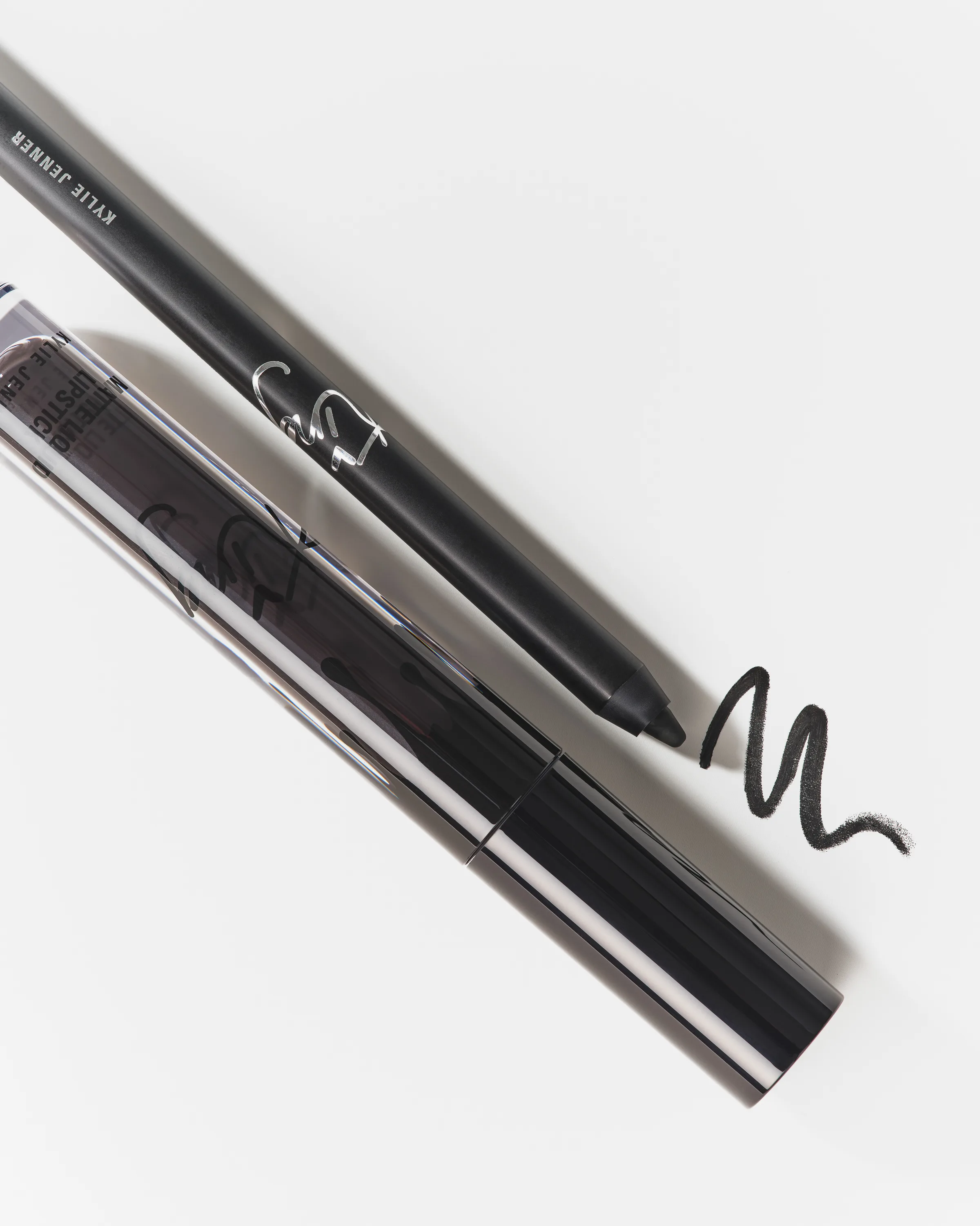 Black lip liner with a swatch beside a chrome lipstick tube on a white background, for Kylie Cosmetics.