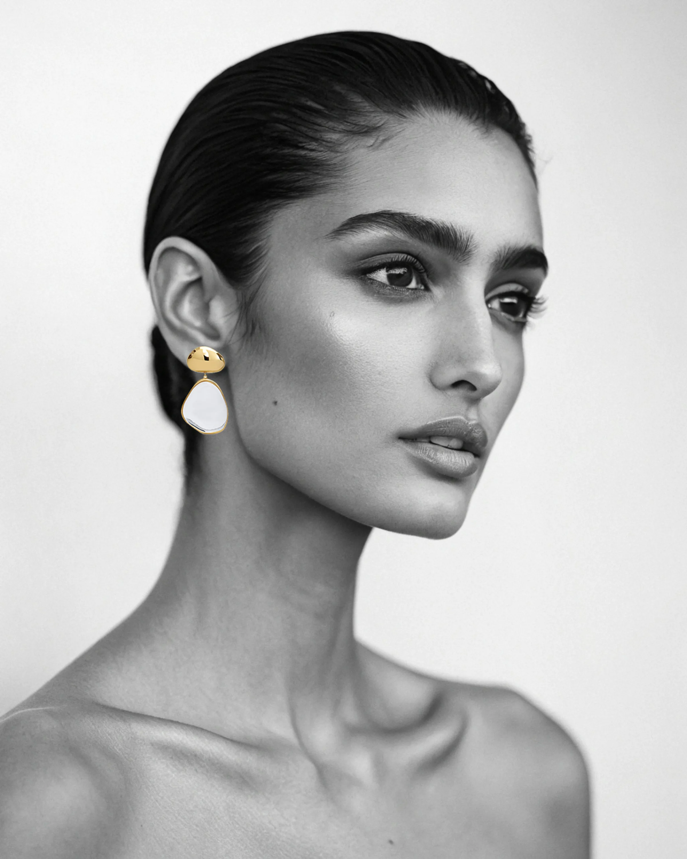 AI image of a model in black and white wearing a gold and white enamel drop earring. Alaïa AI Concept.