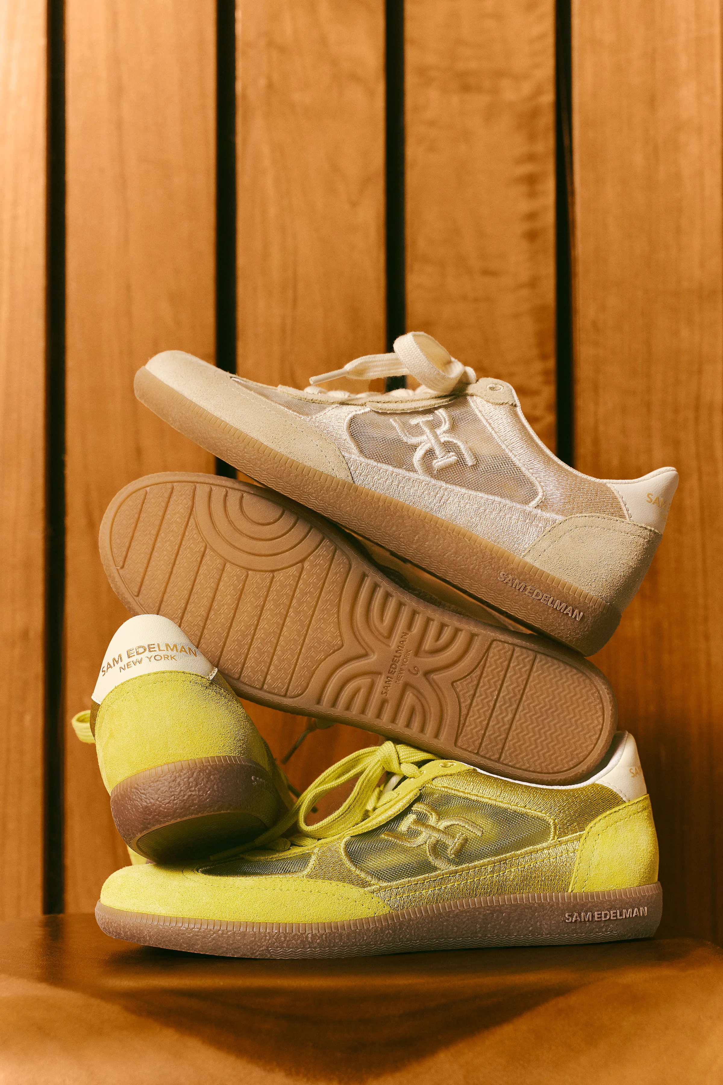 Cream and chartreuse suede sneakers with gum soles stacked against warm wood slats, for Sam Edelman.