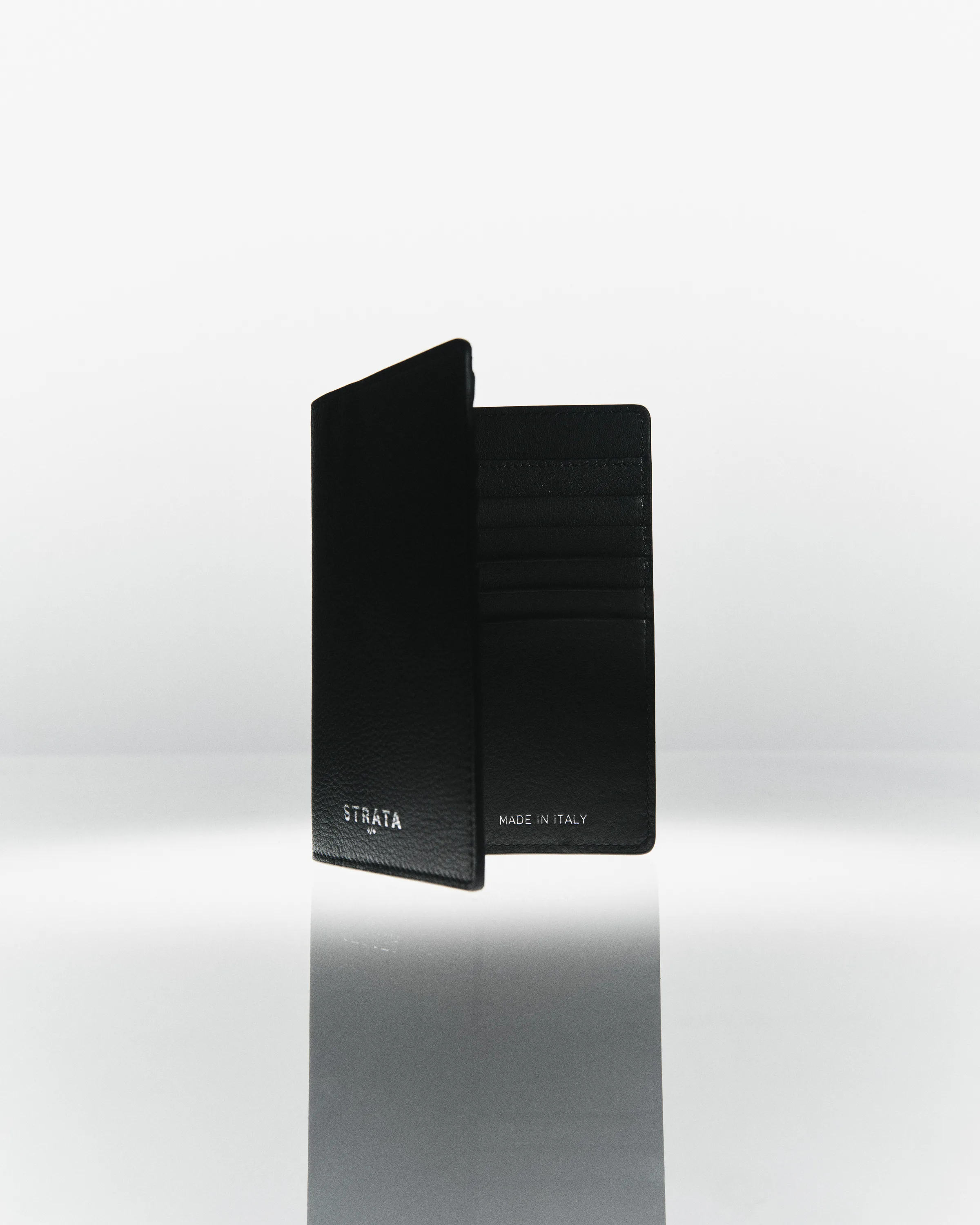 Black pebbled leather travel sleeve standing open with card slots, reflected on a glossy grey surface, for Strata.