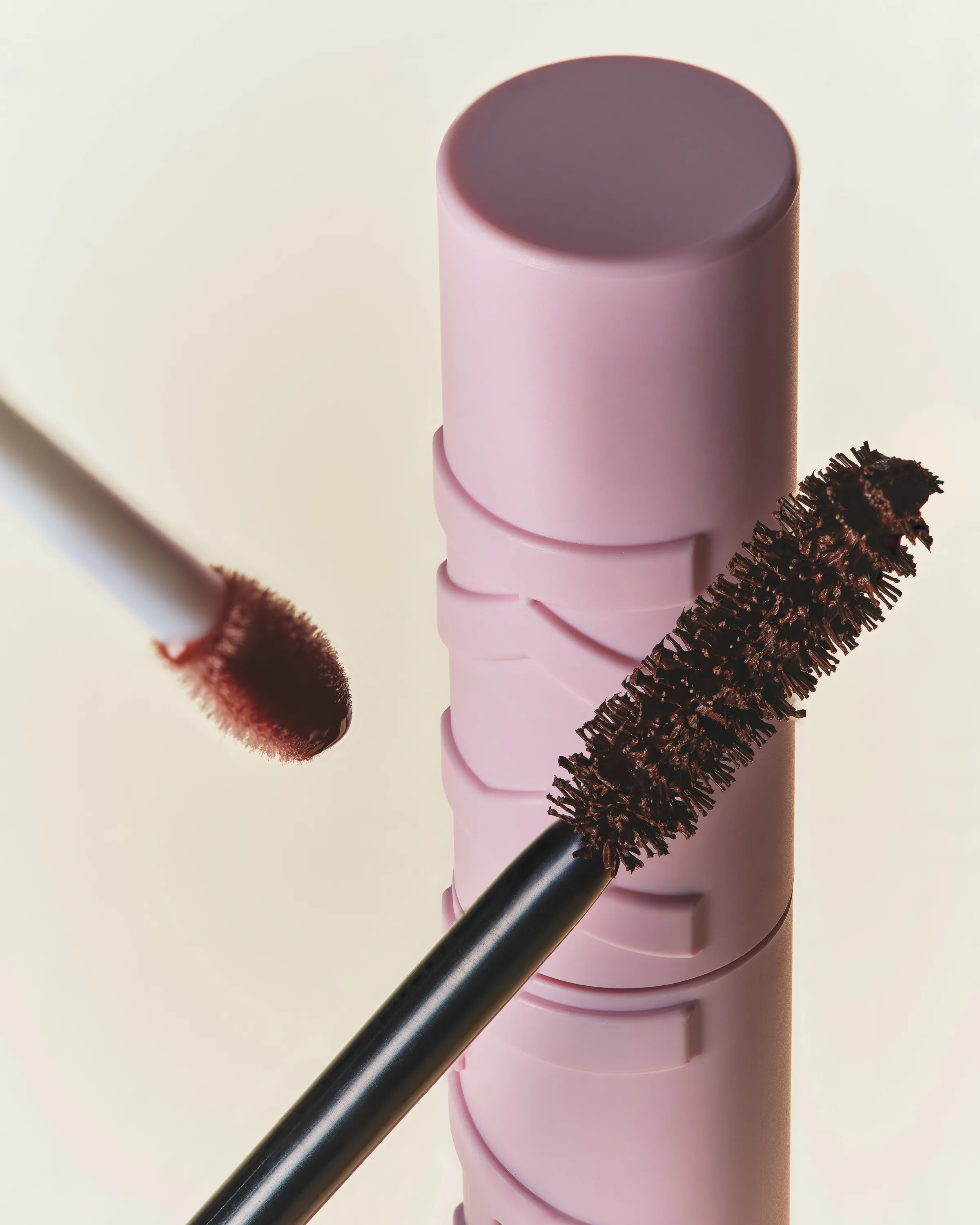 Brown mascara wand beside a pink Kylash tube and a lip applicator on a cream background, for Kylie Cosmetics.