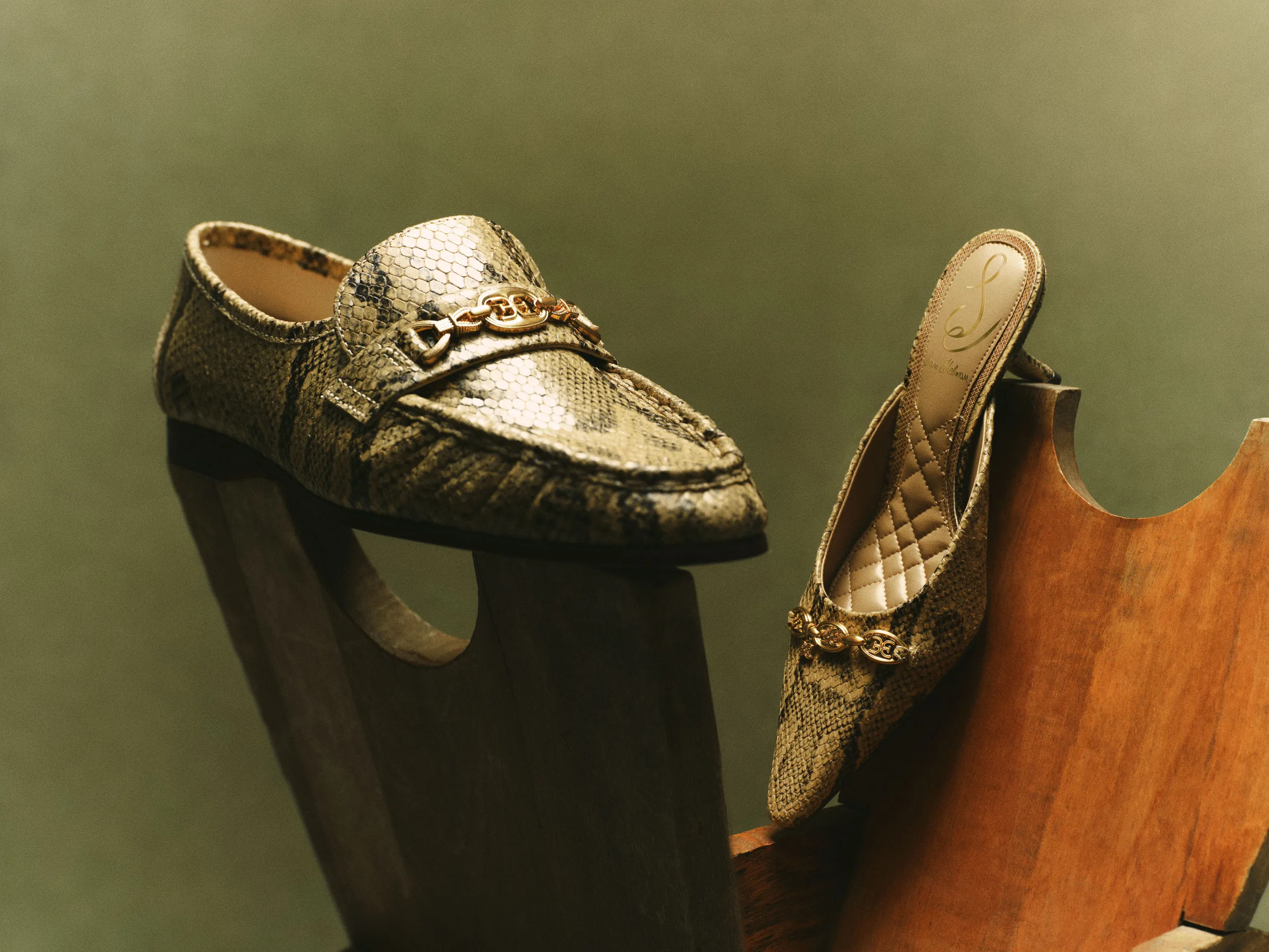 Golden tan snake-print loafer and quilted mule with gold chain hardware on wooden props against olive green, for Sam Edelman.