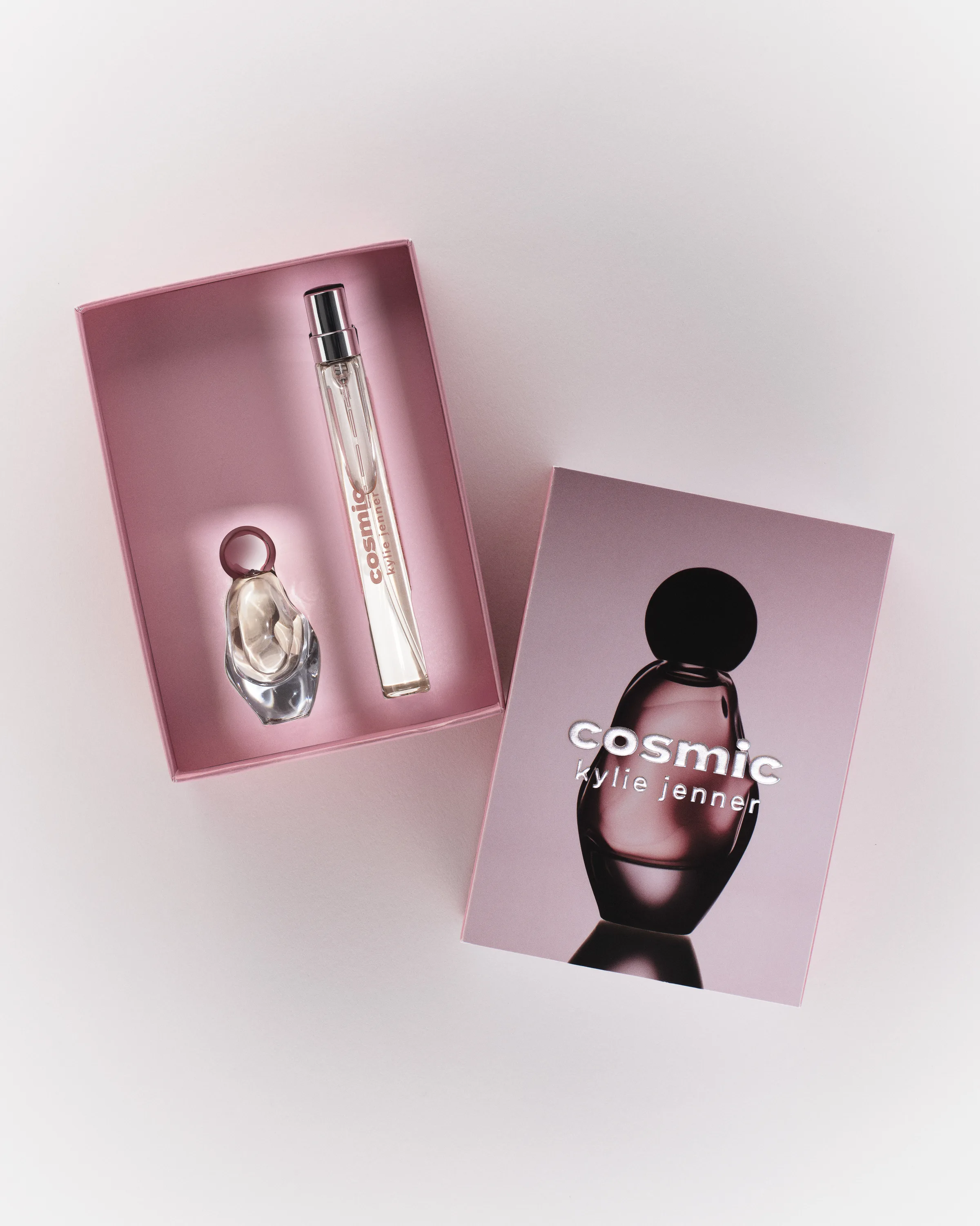 Open pink gift box with Cosmic Kylie Jenner perfume mini and travel spray beside its printed lid, for Kylie Cosmetics.