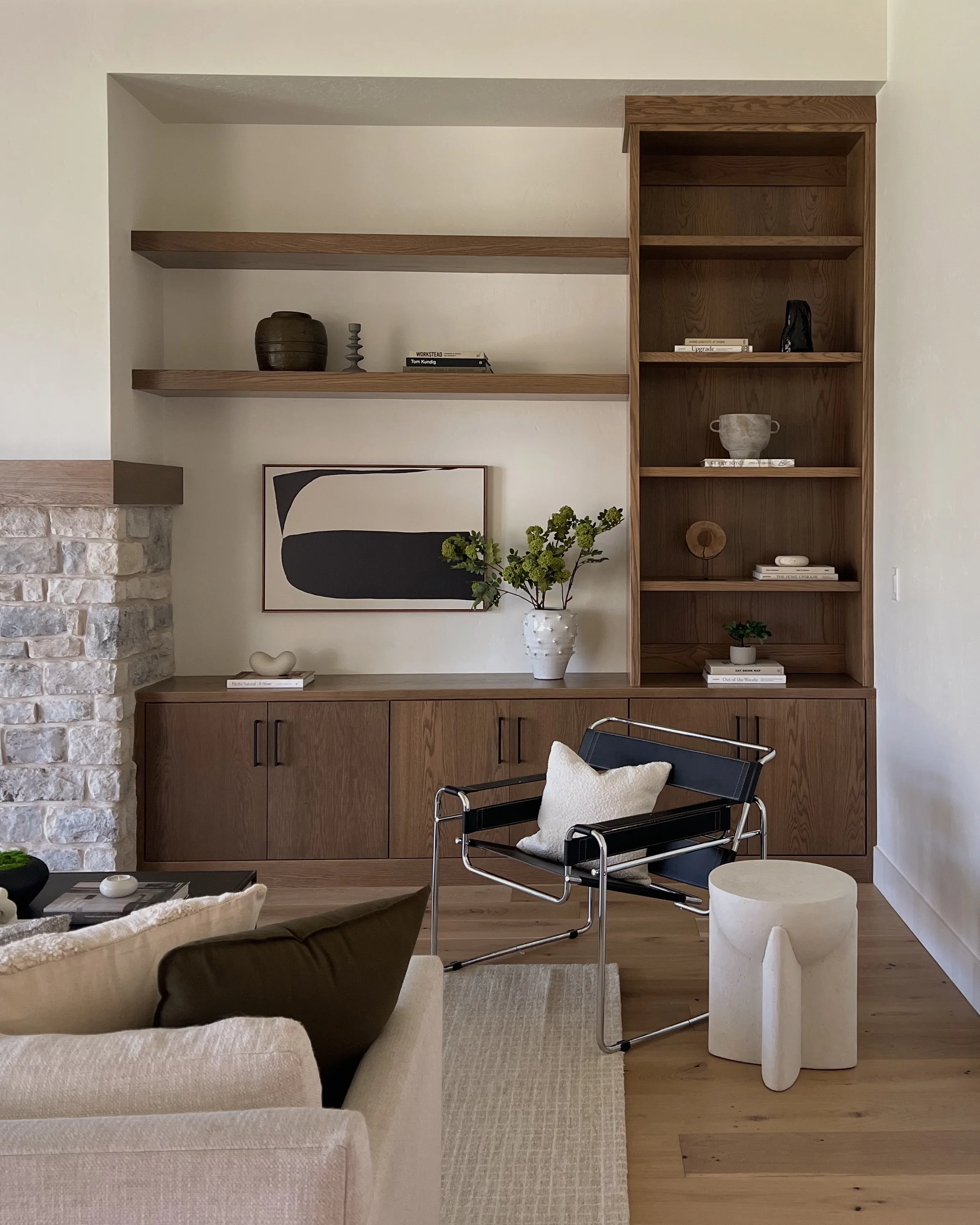 Living room with oak built-in shelves, black leather sling chair, white side table and stone fireplace.