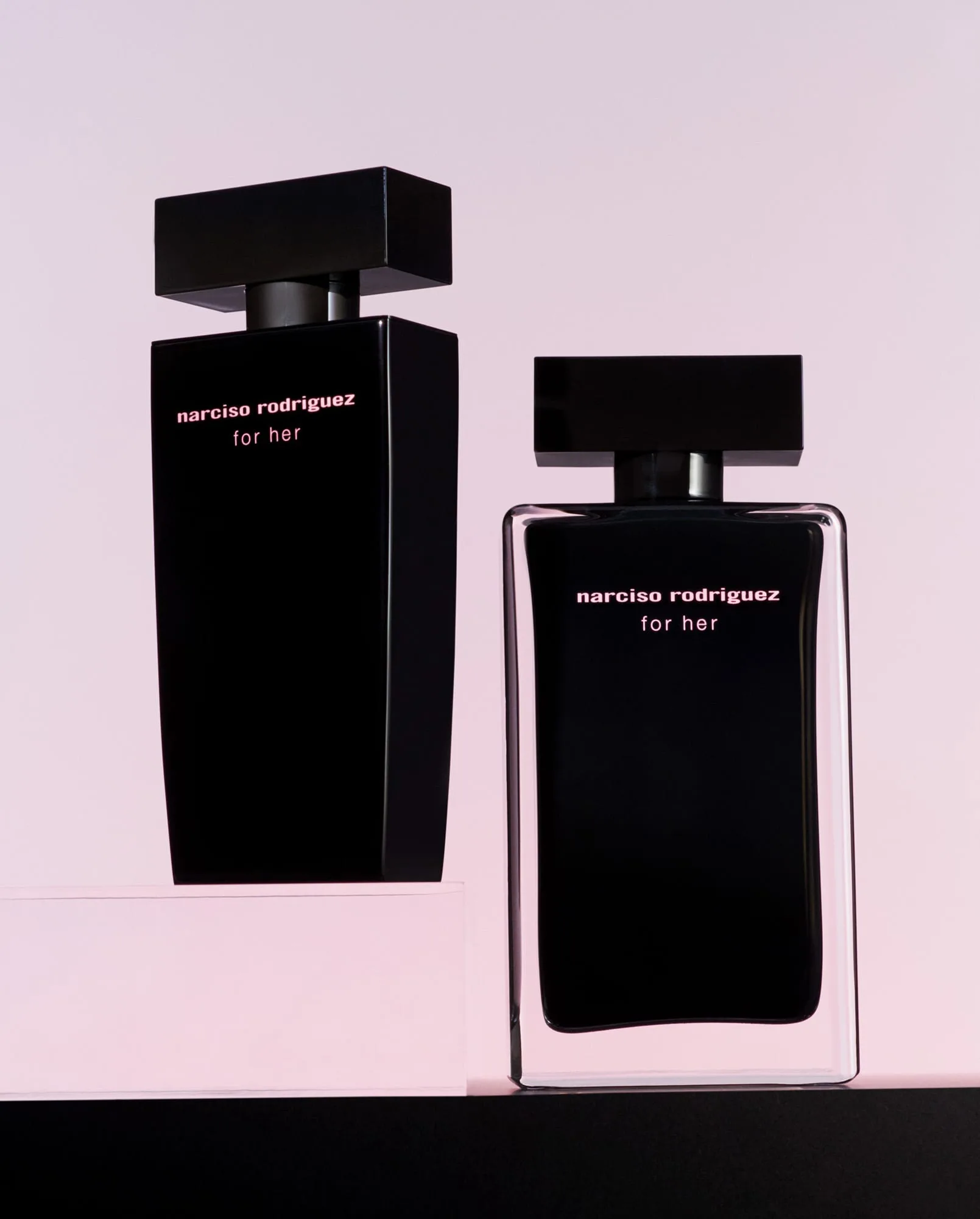 Two black For Her perfume bottles on pink and black plinths against a soft pink backdrop, for Narciso Rodriguez.