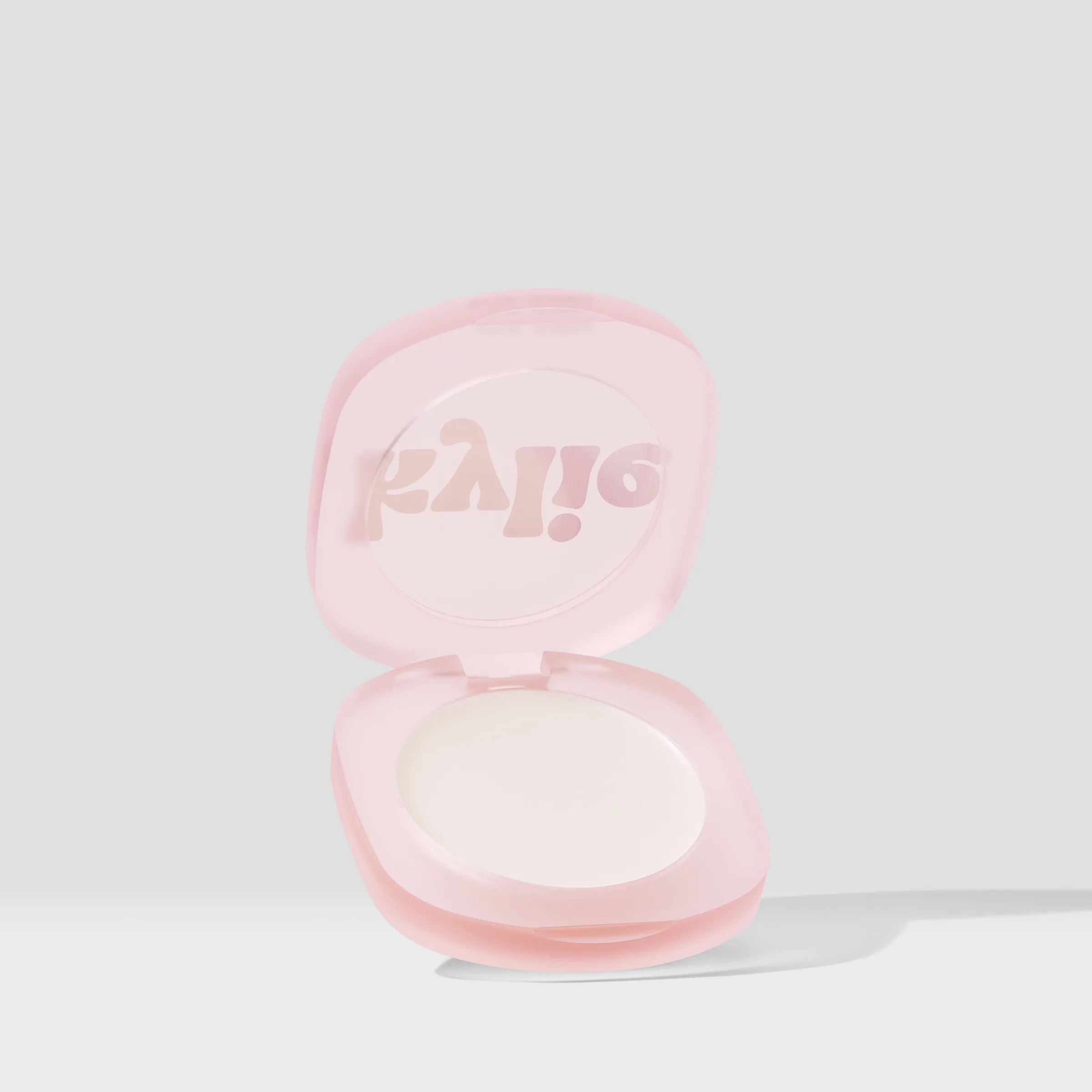 Open frosted pink compact with a white balm pan and embossed kylie lid on a light grey background, for Kylie Cosmetics.
