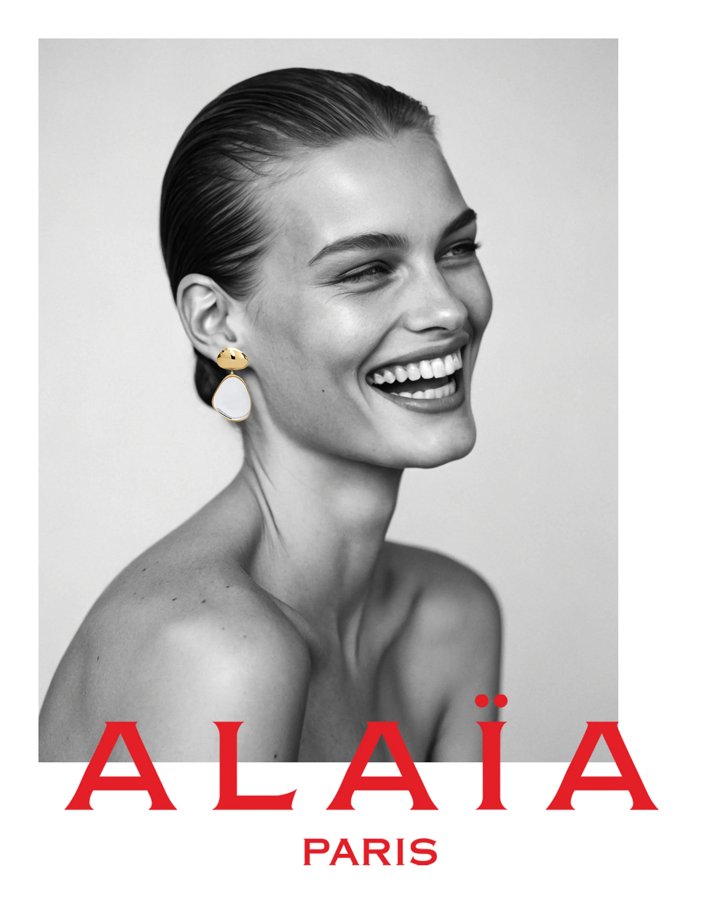 AI image of a laughing model with slicked-back hair and a gold and white drop earring, in black and white. Alaïa AI Concept.