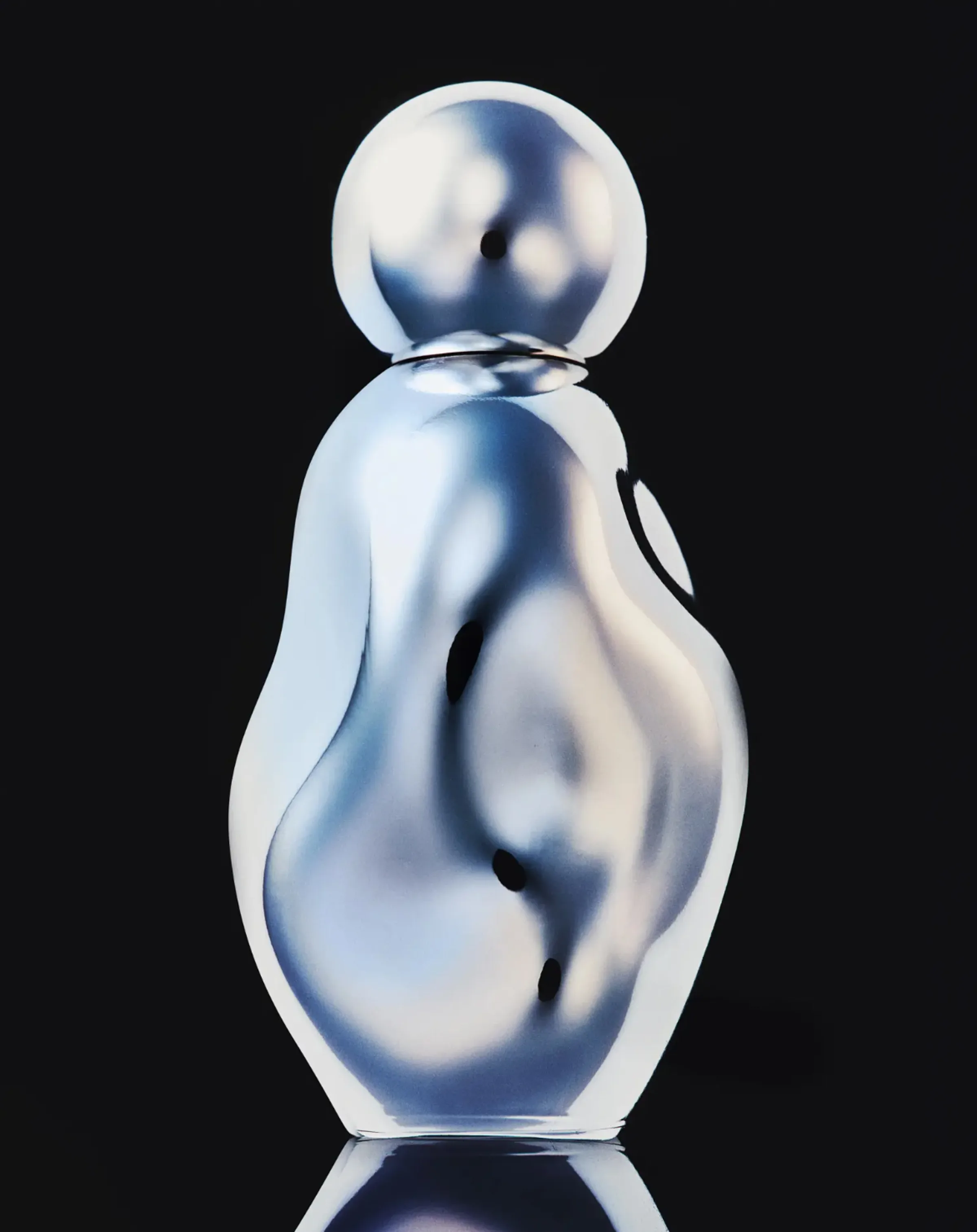 Organic chrome perfume bottle with a round cap, reflecting light against a black background, for Kylie Cosmetics.