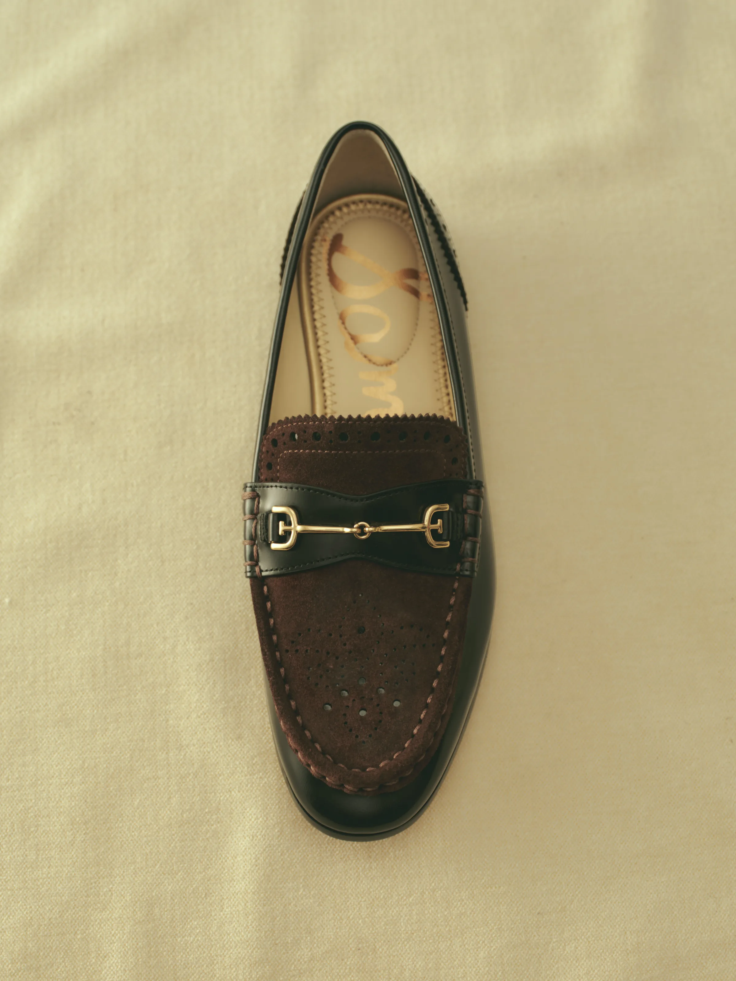 Black leather loafer with burgundy perforated suede and gold horsebit on a cream cloth backdrop, for Sam Edelman.