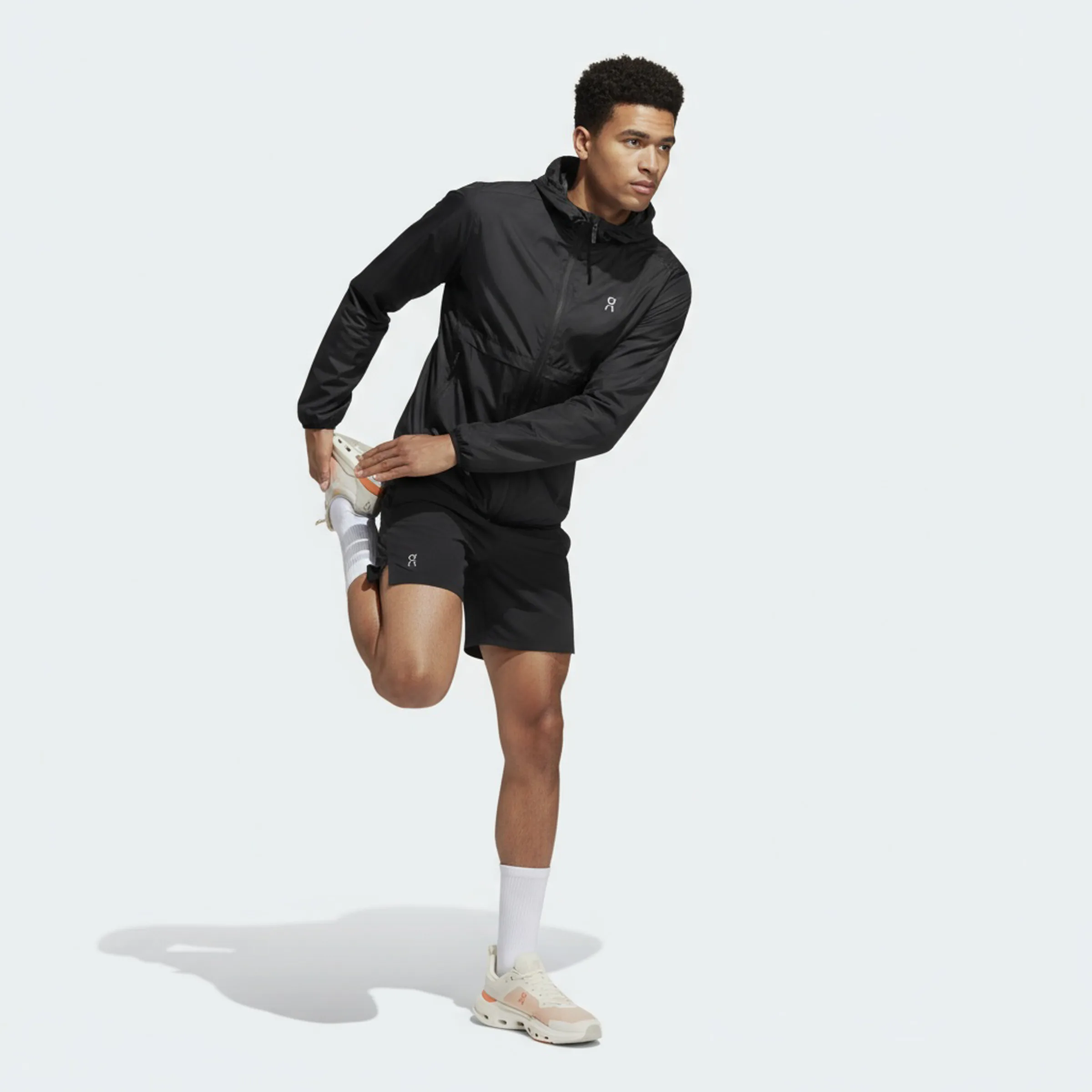AI image of a man stretching his quad in a black hooded running jacket, black shorts and cream sneakers. On AI Concept.