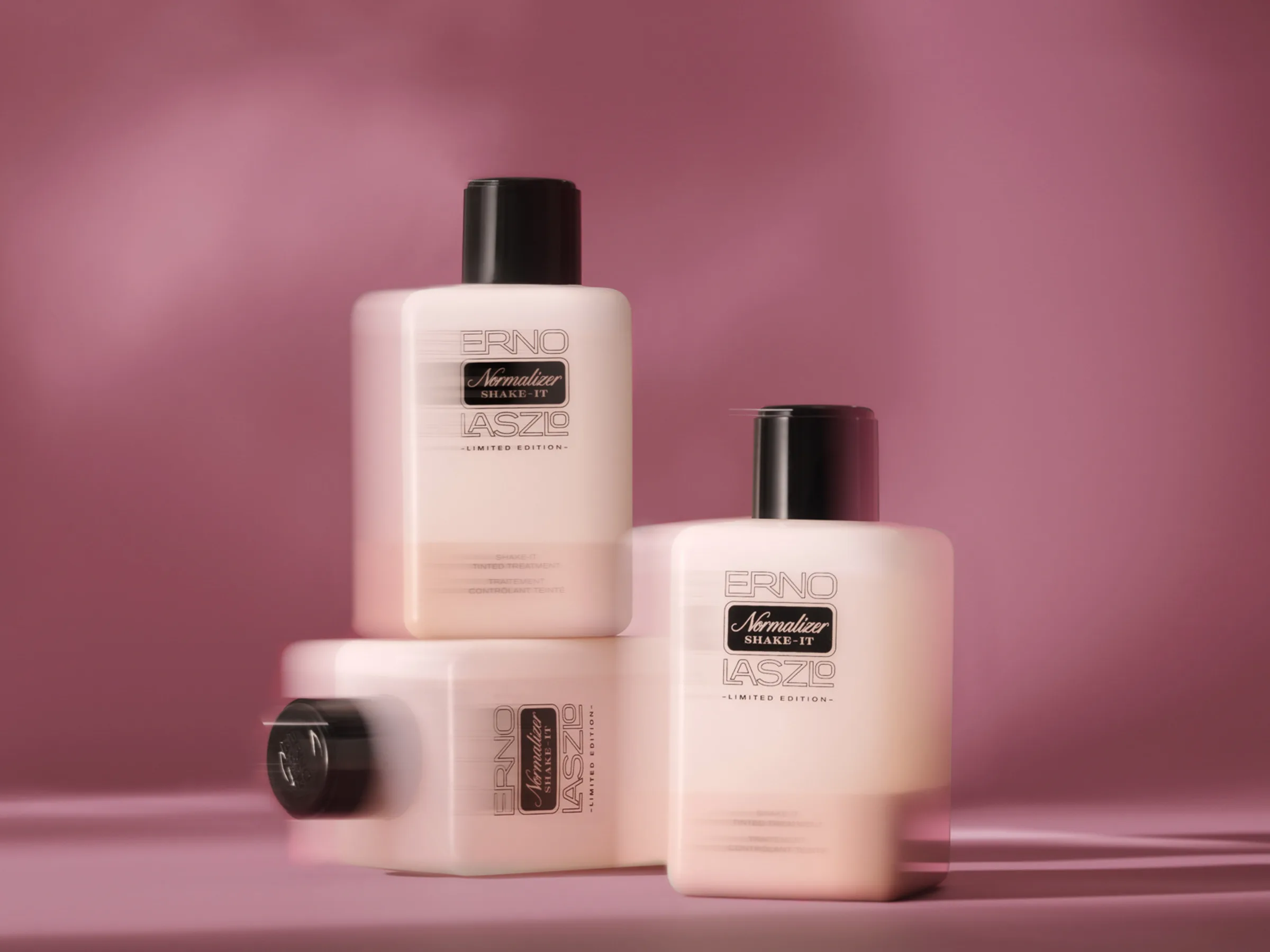 Three limited edition Normalizer Shake-It bottles stacked with motion blur against a mauve pink backdrop, for Erno Laszlo.