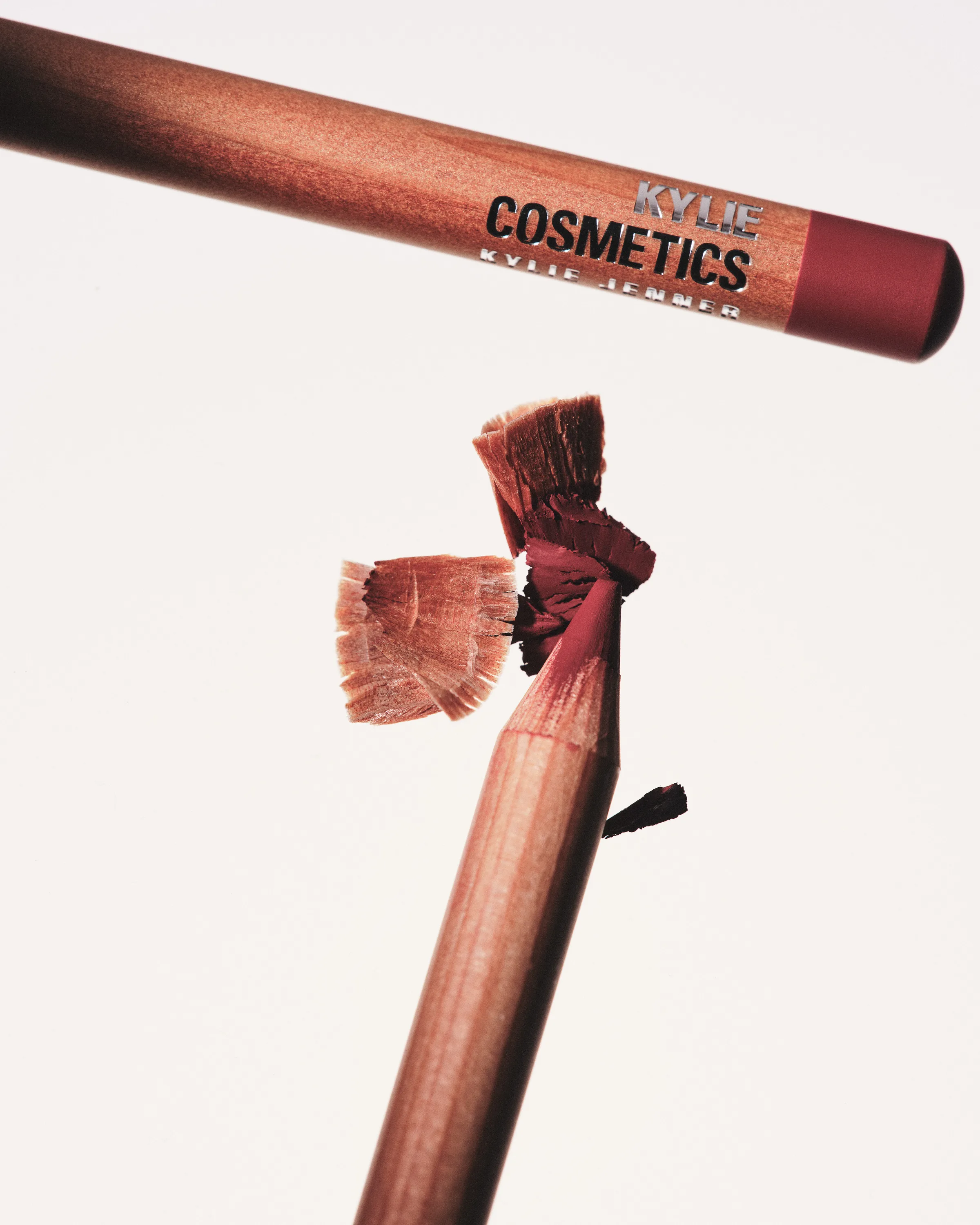 Two mauve lip liner pencils, one freshly sharpened with wood shavings curling off, on a white background, for Kylie Cosmetics.