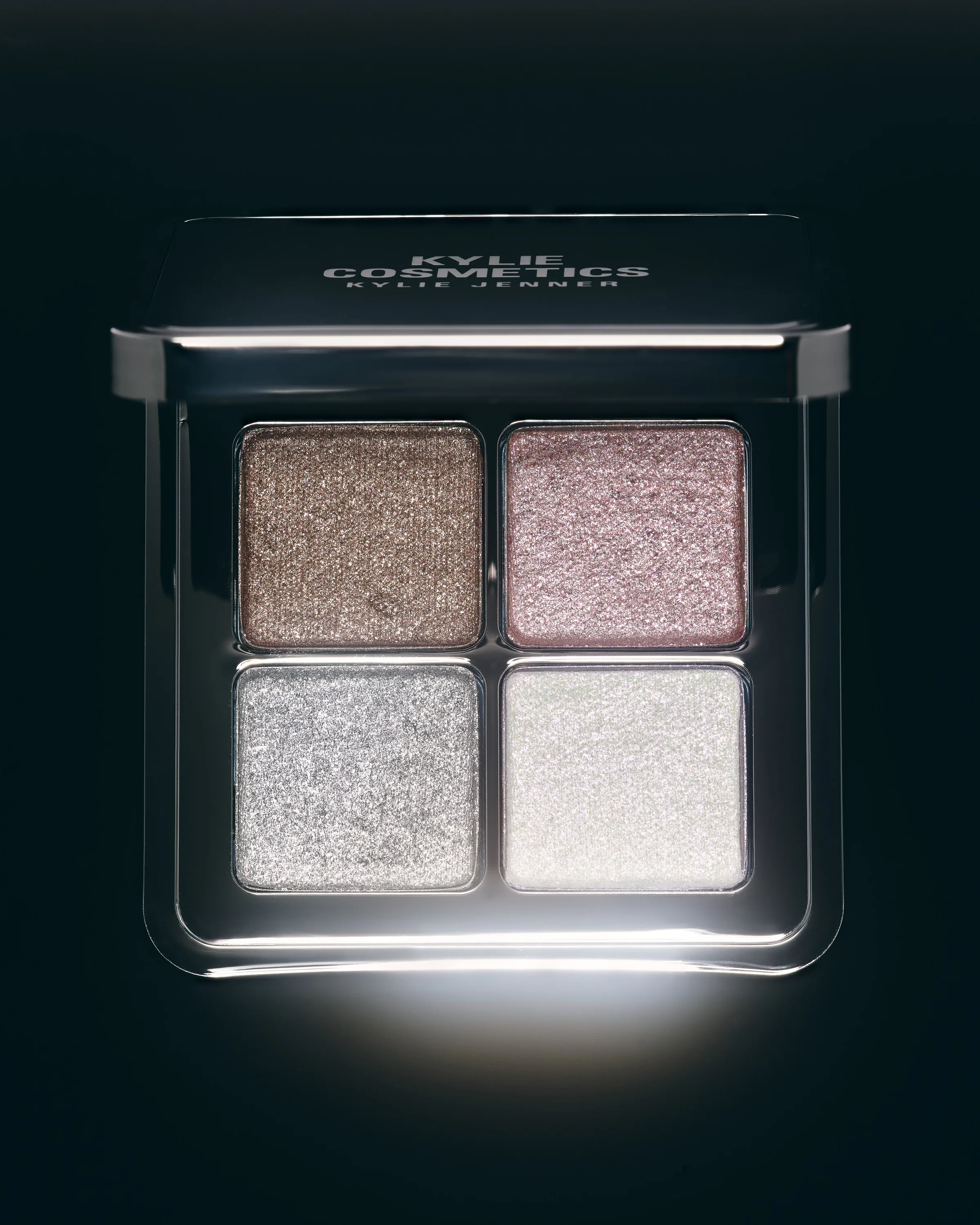 Four-pan shimmer eyeshadow palette in bronze, pink, silver and pearl, lit on a black background, for Kylie Cosmetics.