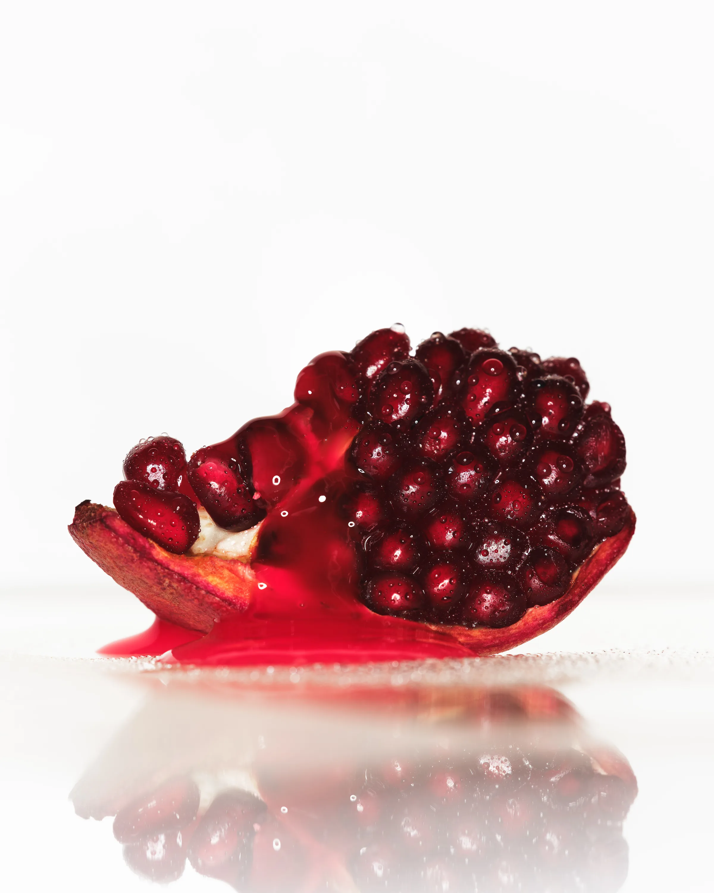 Still life of a pomegranate wedge spilling red juice on a reflective white surface, for Kylie Cosmetics.