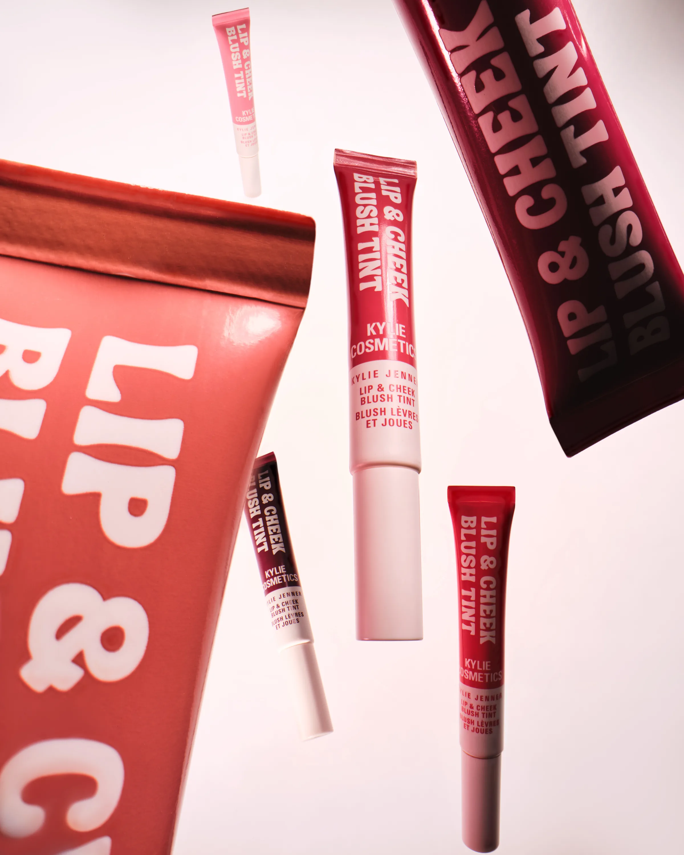 Lip & Cheek Blush Tint tubes in pink and berry shades floating against a white background, for Kylie Cosmetics.