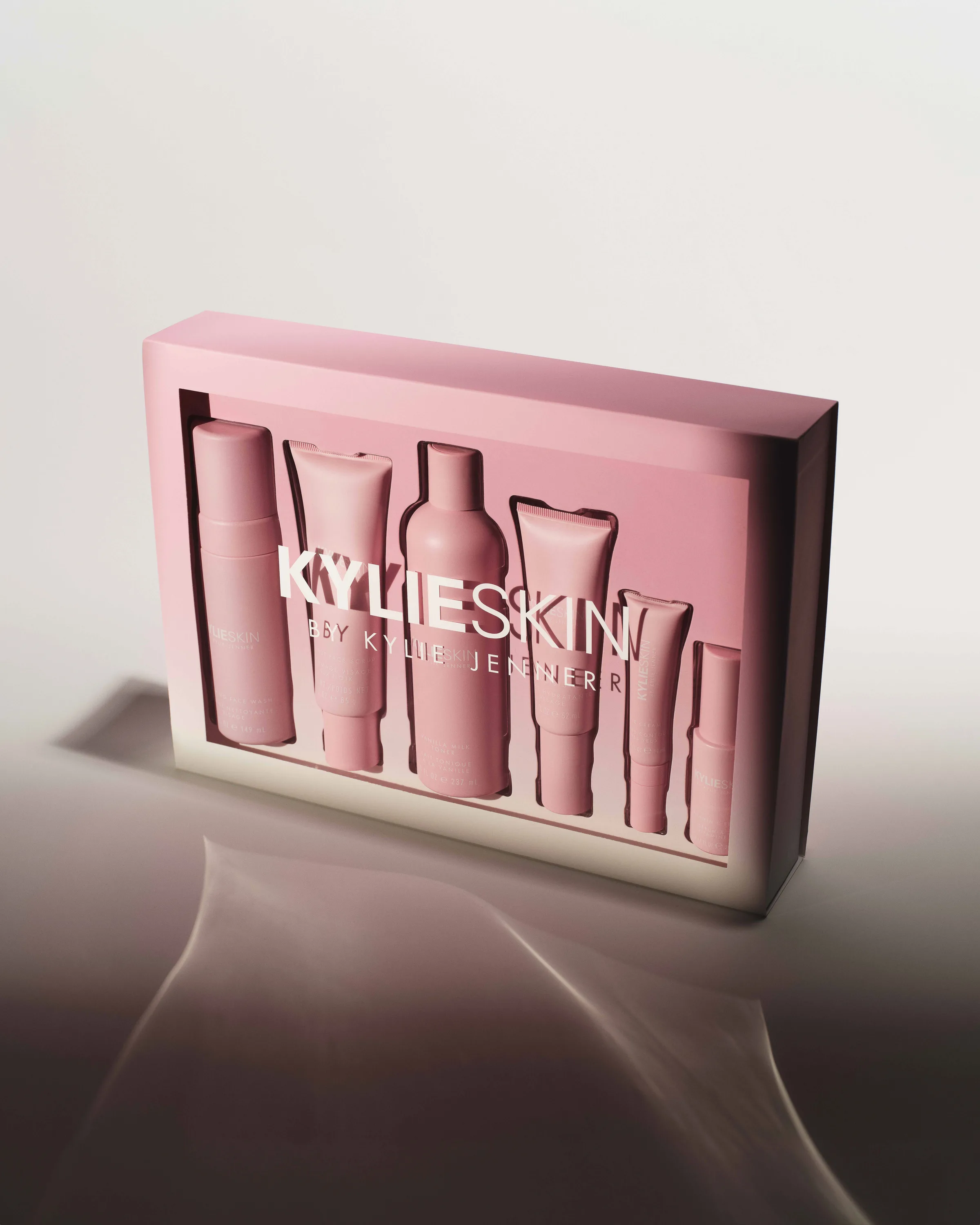 Pink Kylie Skin gift box with six skincare products behind a clear logo window, lit on a glossy surface, for Kylie Cosmetics.