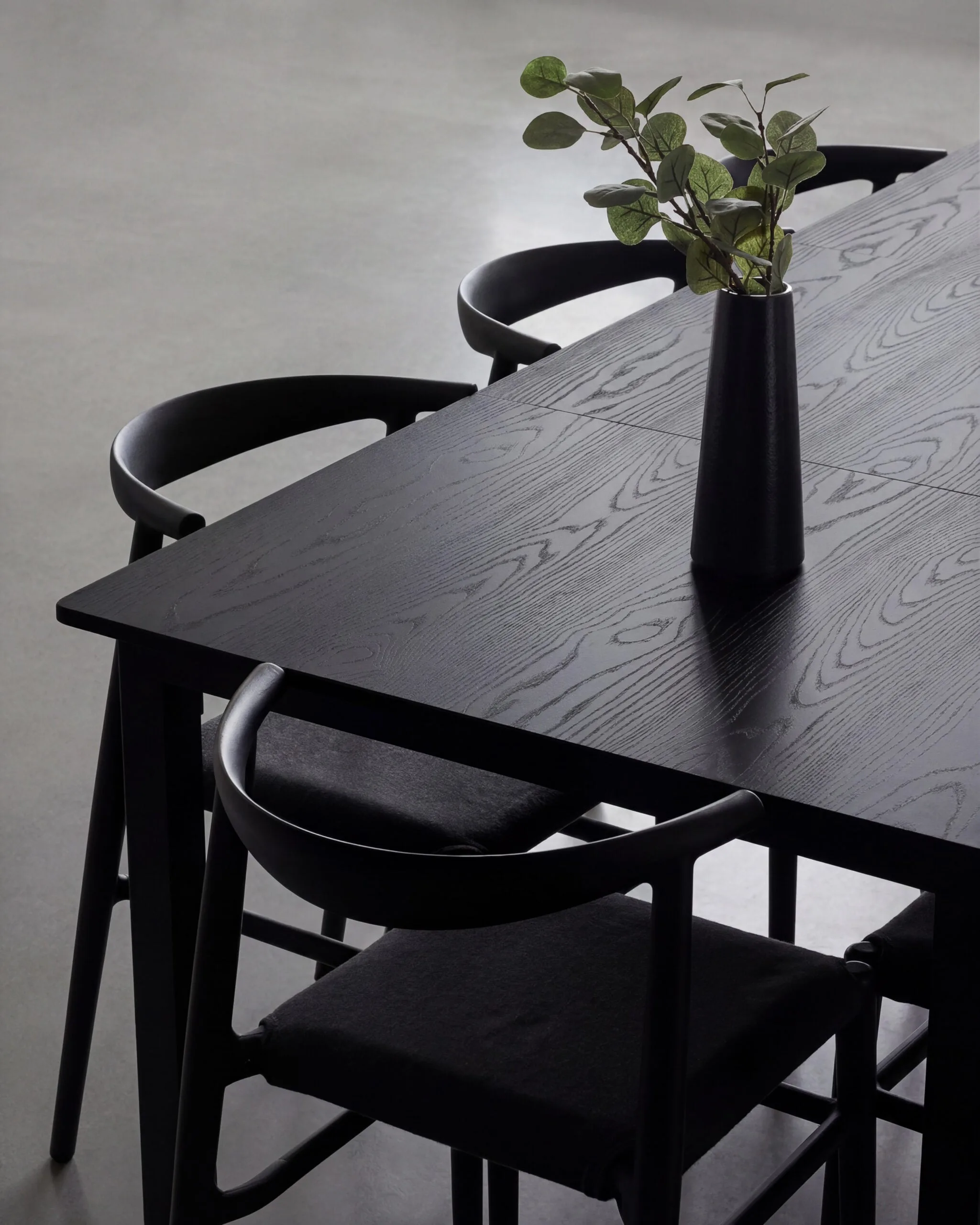 Black oak dining table with curved black chairs and a eucalyptus vase on a grey concrete floor at Studio 1 in Long Island City.