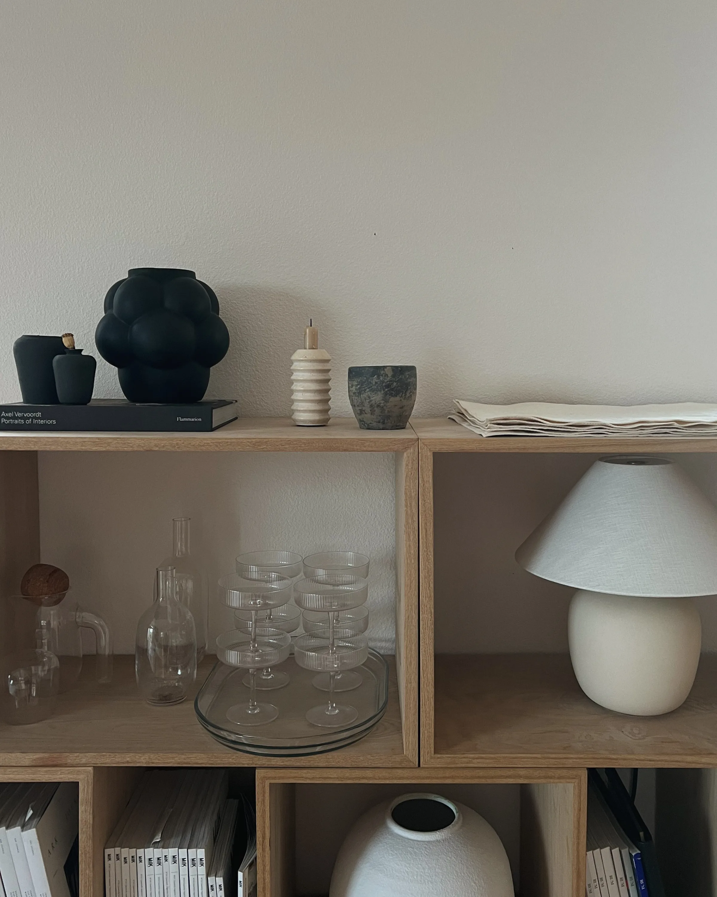 Oak cube shelves styled with black vases, ribbed glassware, a linen-shade ceramic lamp and stacked books.