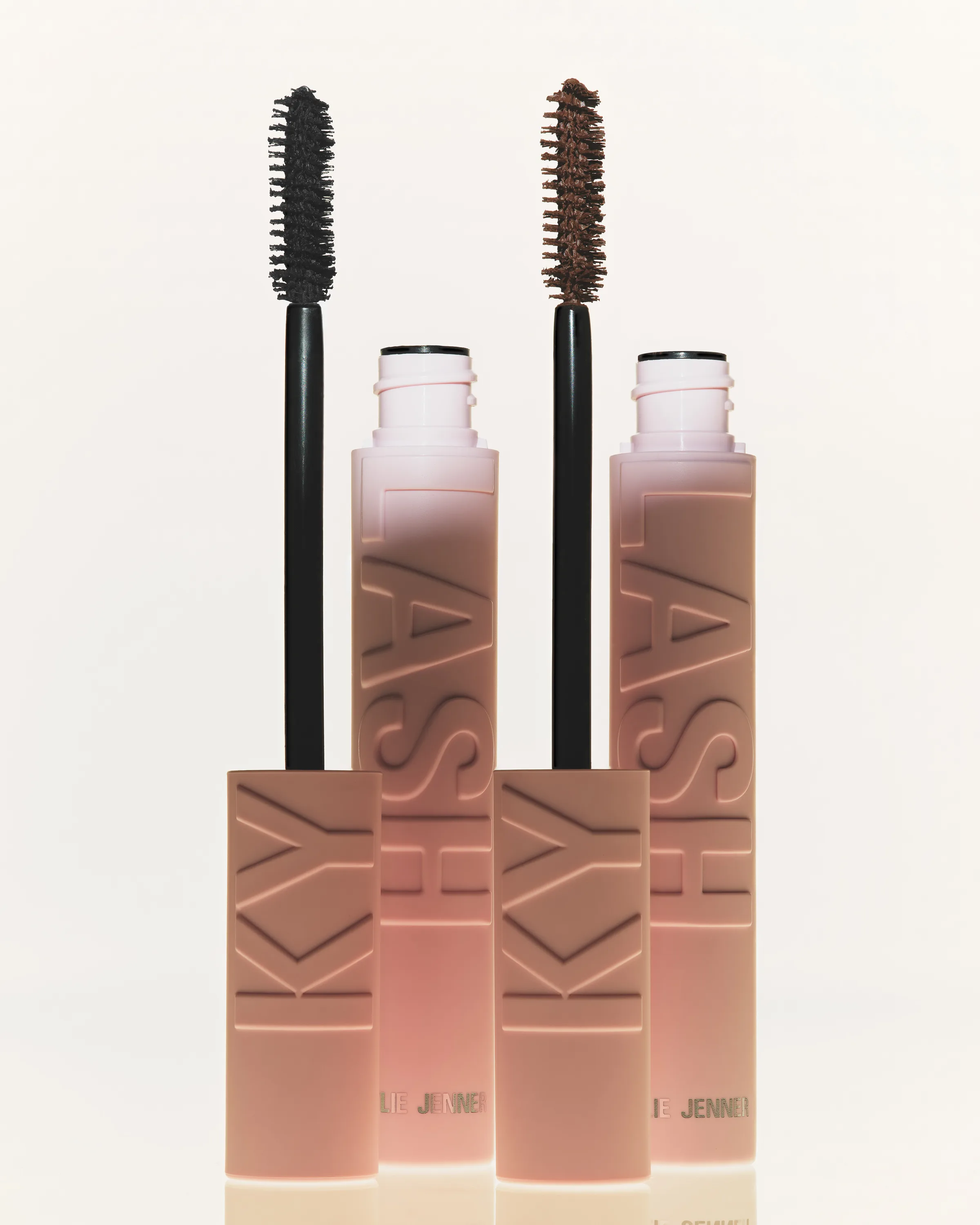 Two open pink Kylash mascara tubes with black and brown wands standing upright on a cream backdrop, for Kylie Cosmetics.