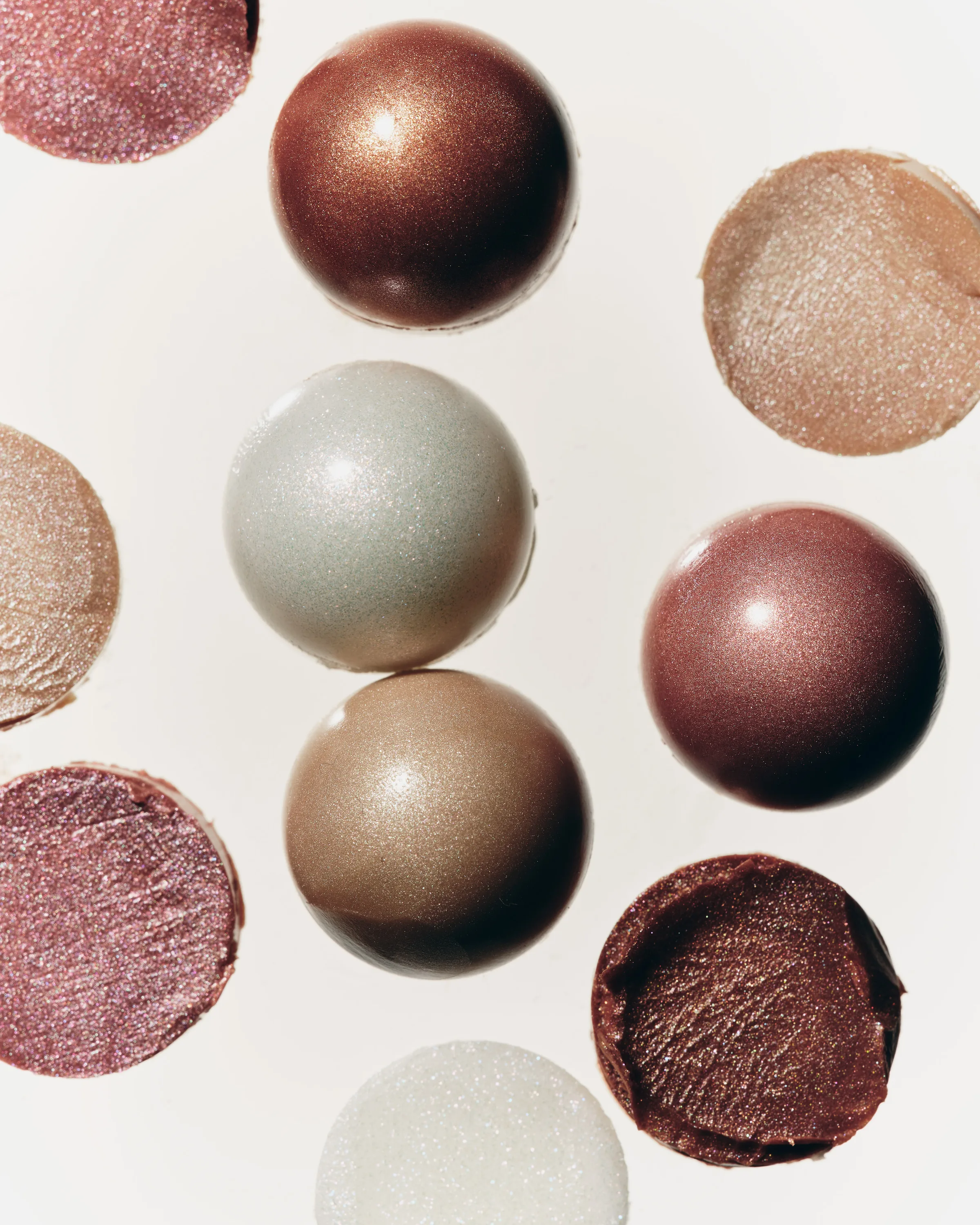 Still life of shimmering dewy balm spheres and swatches in bronze, pearl and rose shades on white, for Kylie Cosmetics.