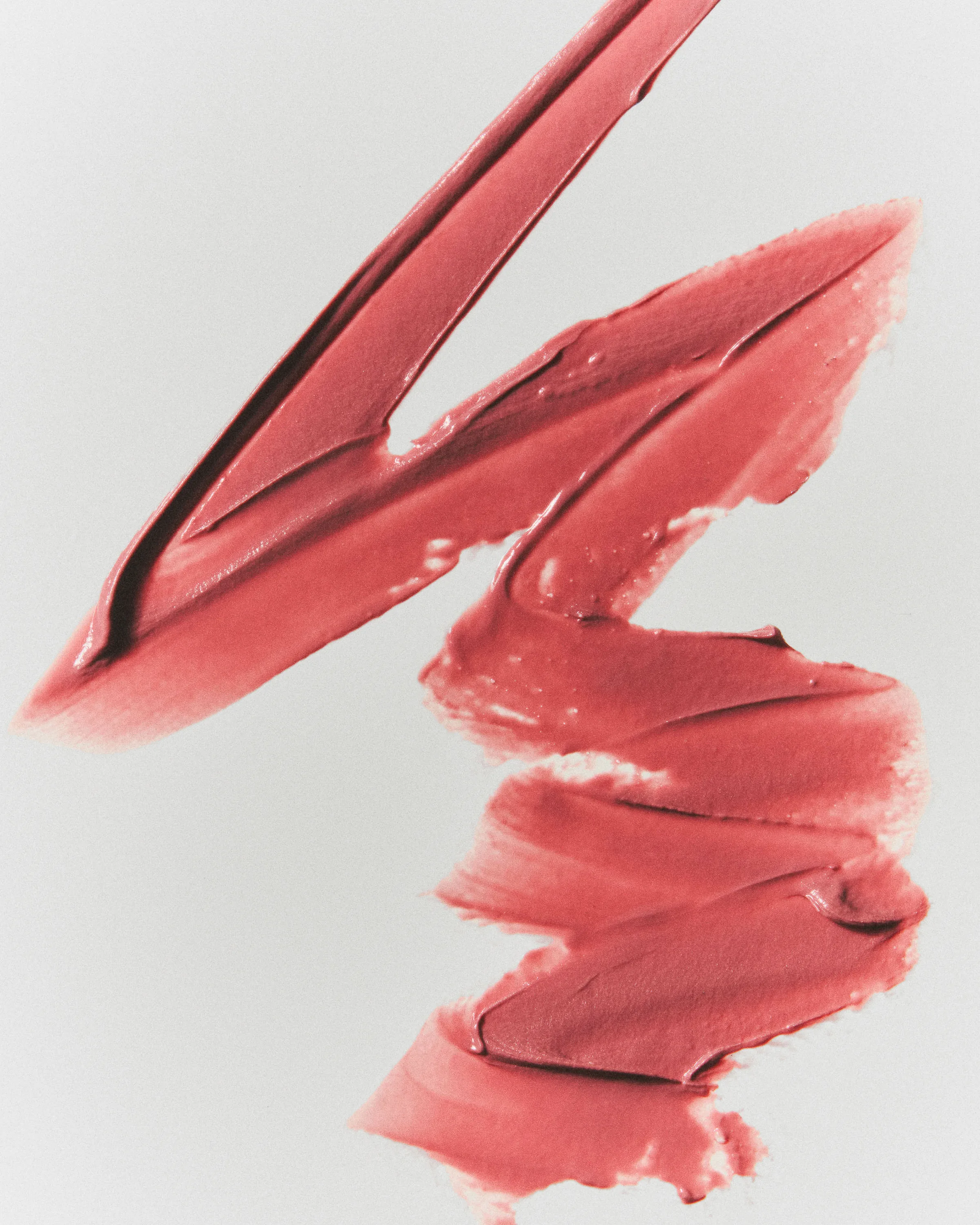 Zigzag swatch of creamy coral-pink lipstick smeared across a pale grey background, for Kylie Cosmetics.