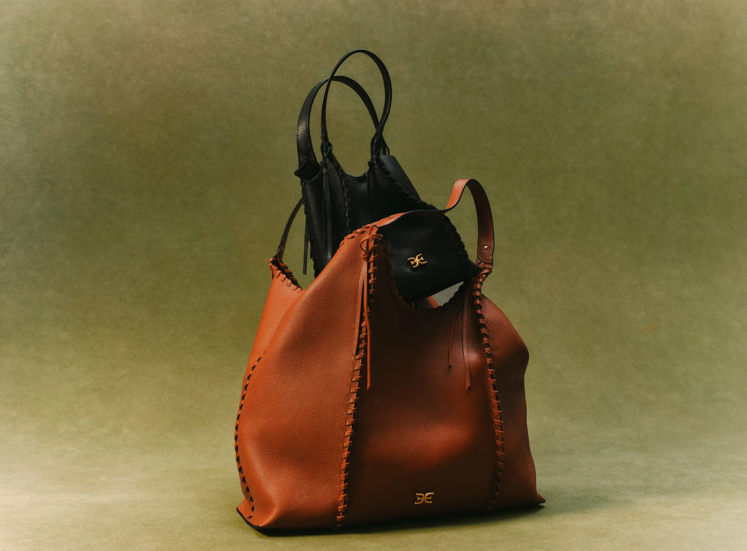 Black whipstitch crossbody tote tucked inside a cognac leather expandable tote on an olive backdrop, for Sam Edelman.