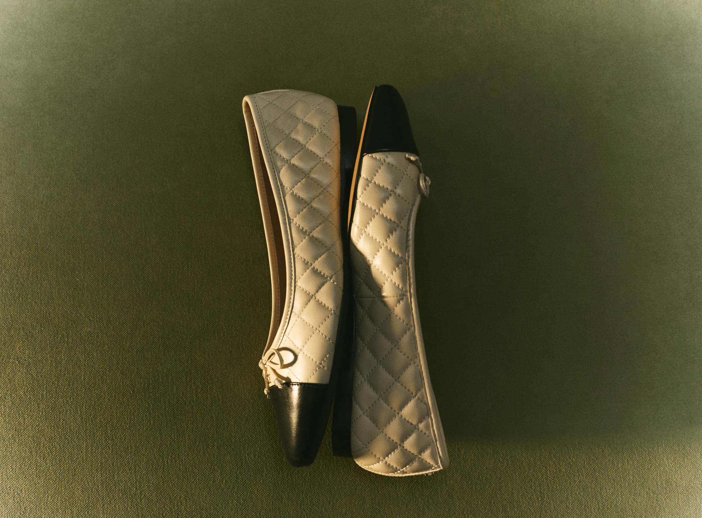Quilted silver ballet flats with black cap toes and logo charms on a sage green backdrop, for Sam Edelman.
