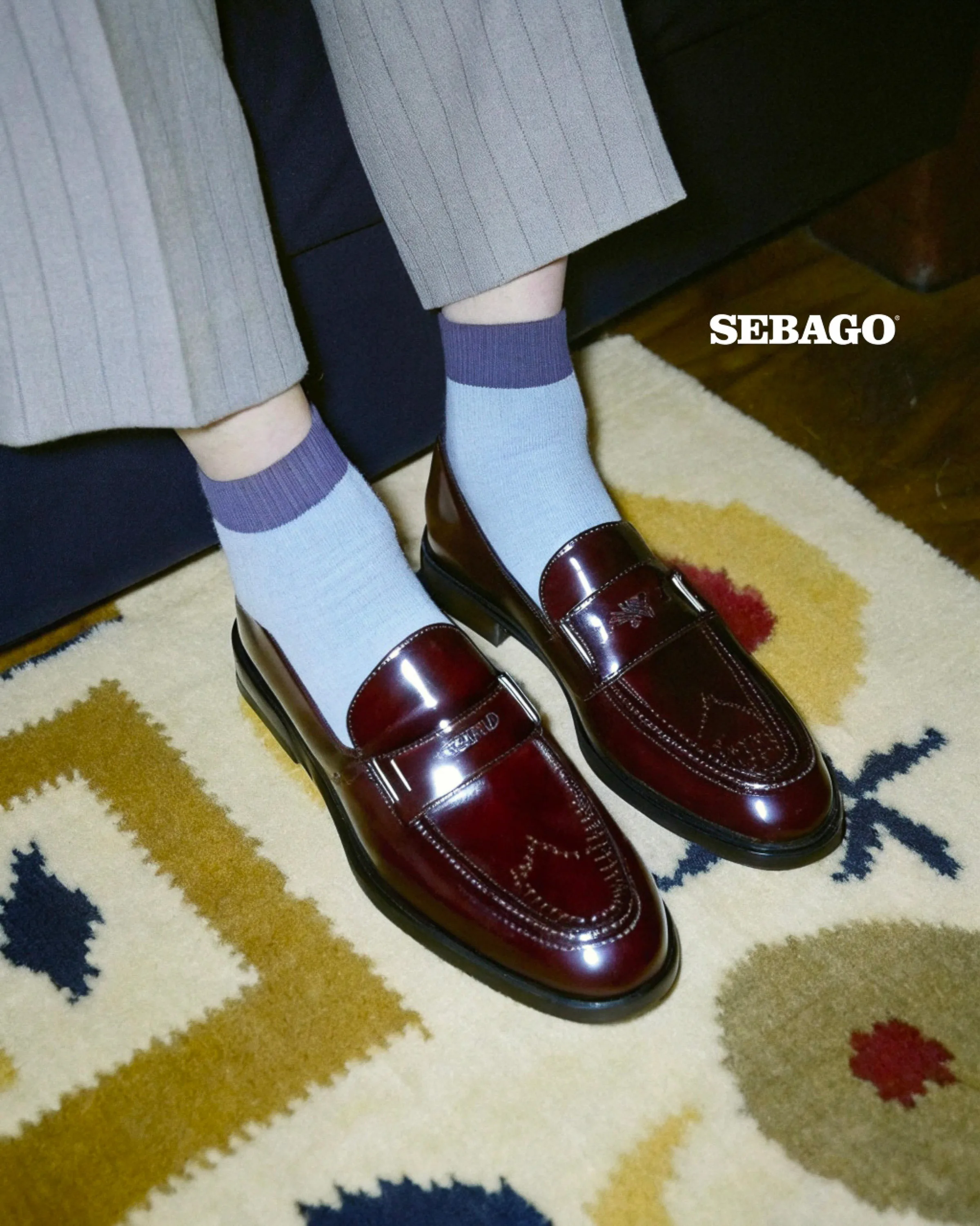 AI image of burgundy patent leather loafers worn with light blue socks on a patterned wool rug. Sebago AI Concept.