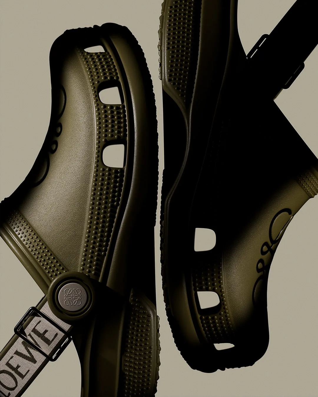 CGI render of two olive green clogs with embossed anagram and logo strap on a beige background, for Loewe.