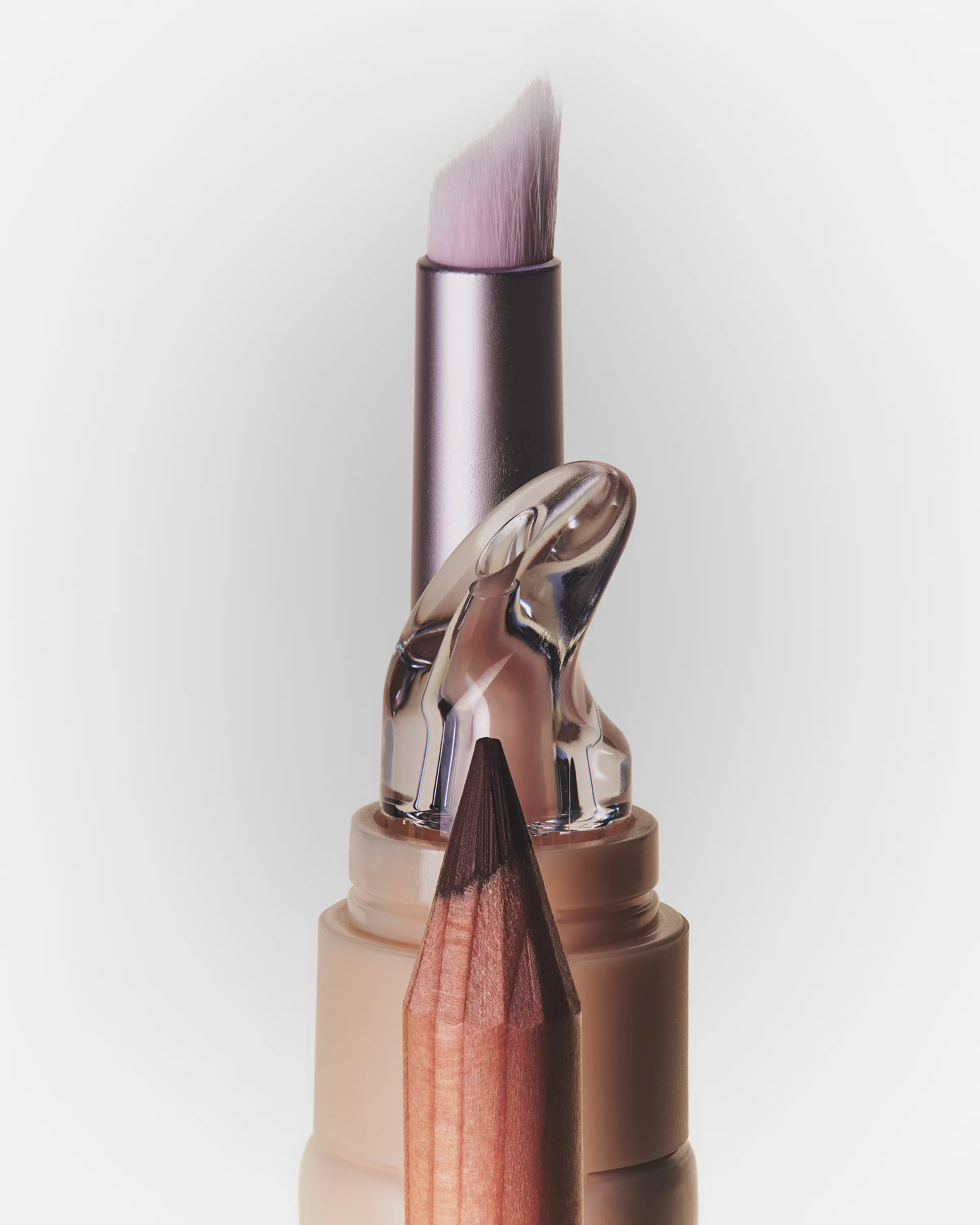 Still life of a lip brush, clear lip butter applicator and lip pencil tip stacked on a pale backdrop, for Kylie Cosmetics.