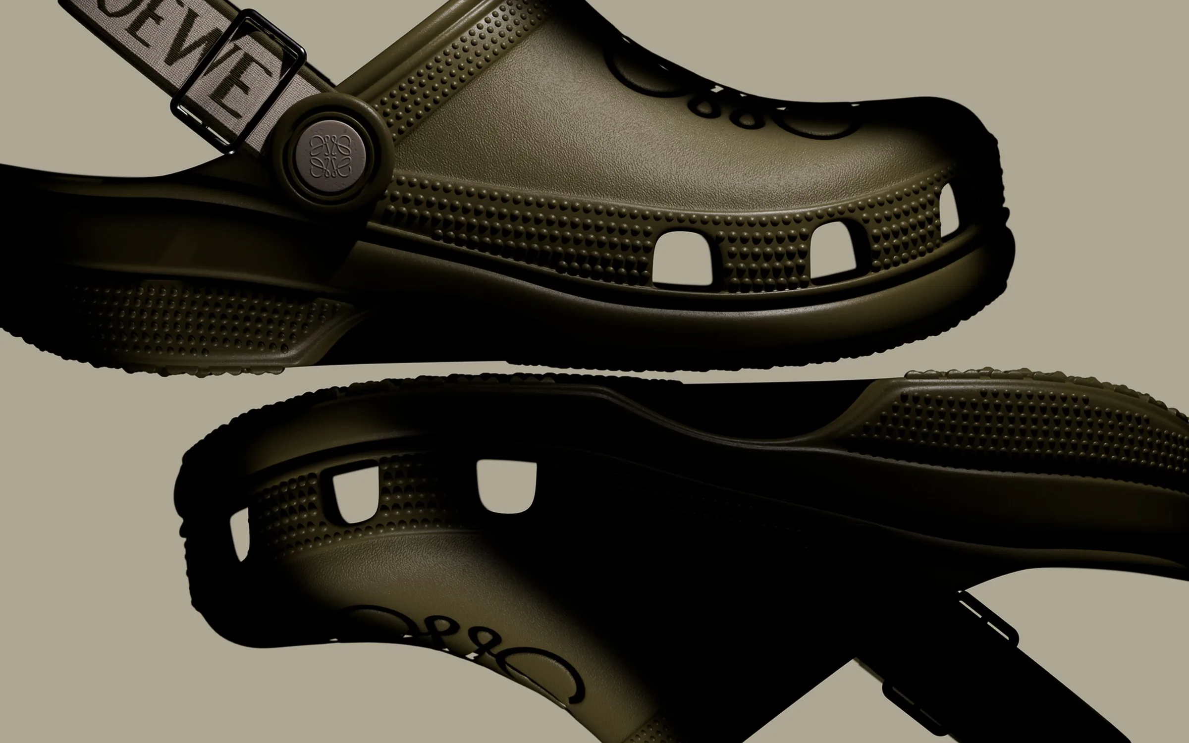 CGI render of two olive green clogs with an anagram logo button and LOEWE strap on a taupe background, for Loewe.