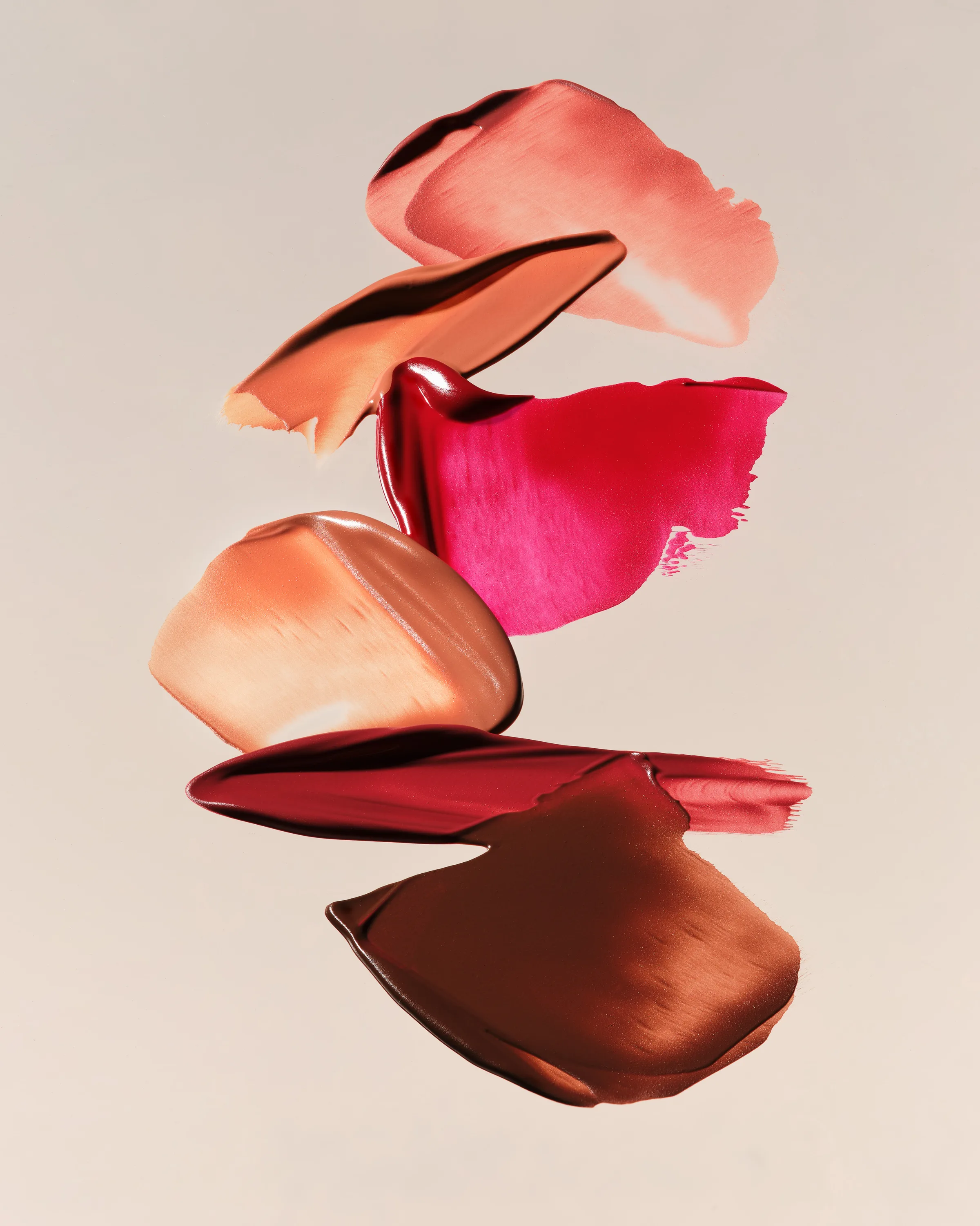 Stacked lipstick swatches in nude, pink, red and brown shades on a beige background, for Kylie Cosmetics.