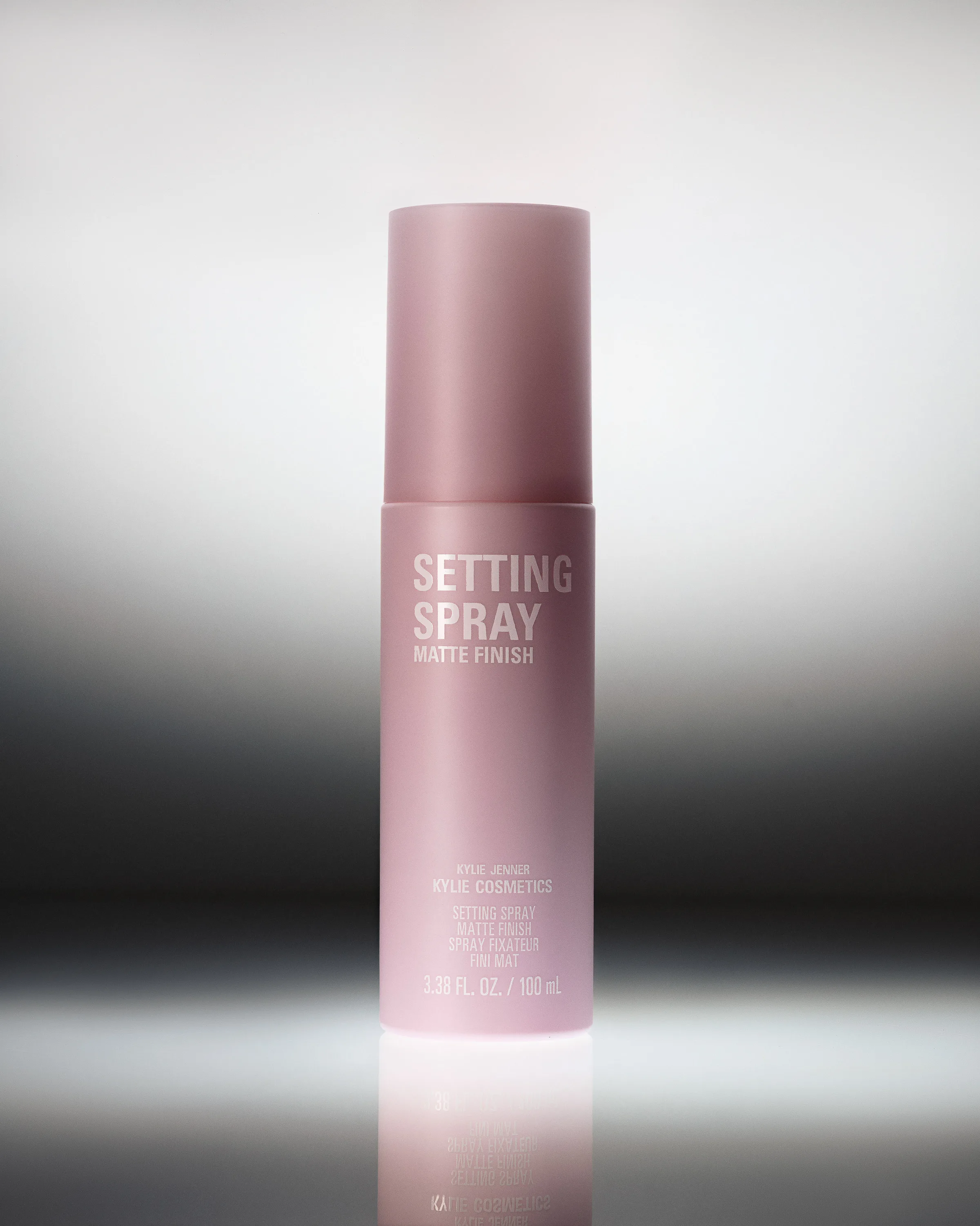 Pink matte finish setting spray bottle on a reflective surface against a silver and black gradient, for Kylie Cosmetics.