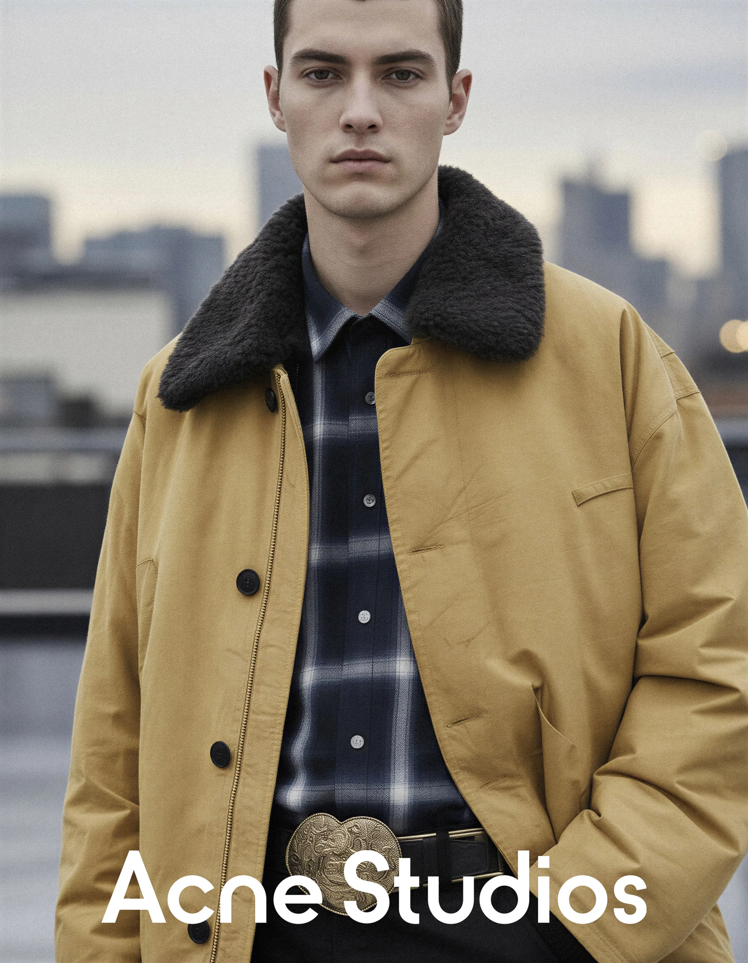 AI image of a man in a mustard jacket with dark shearling collar and plaid shirt on a city rooftop. Acne Studios AI Concept.