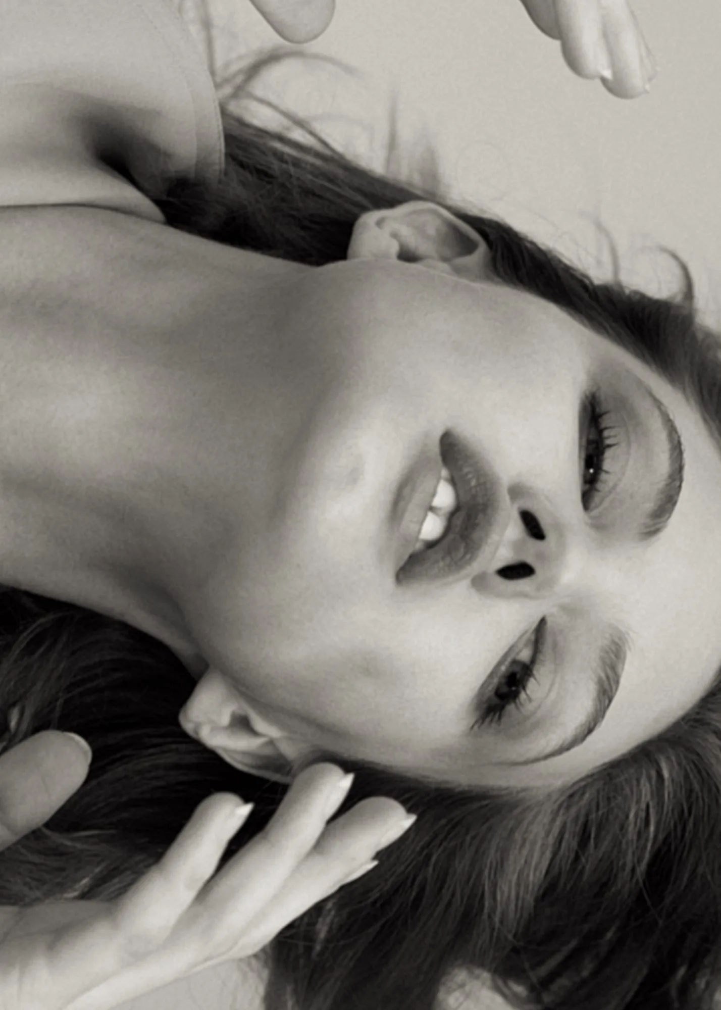 Black and white upside-down portrait of a woman lying back with hair spread and hands near her face, for Puss Puss.