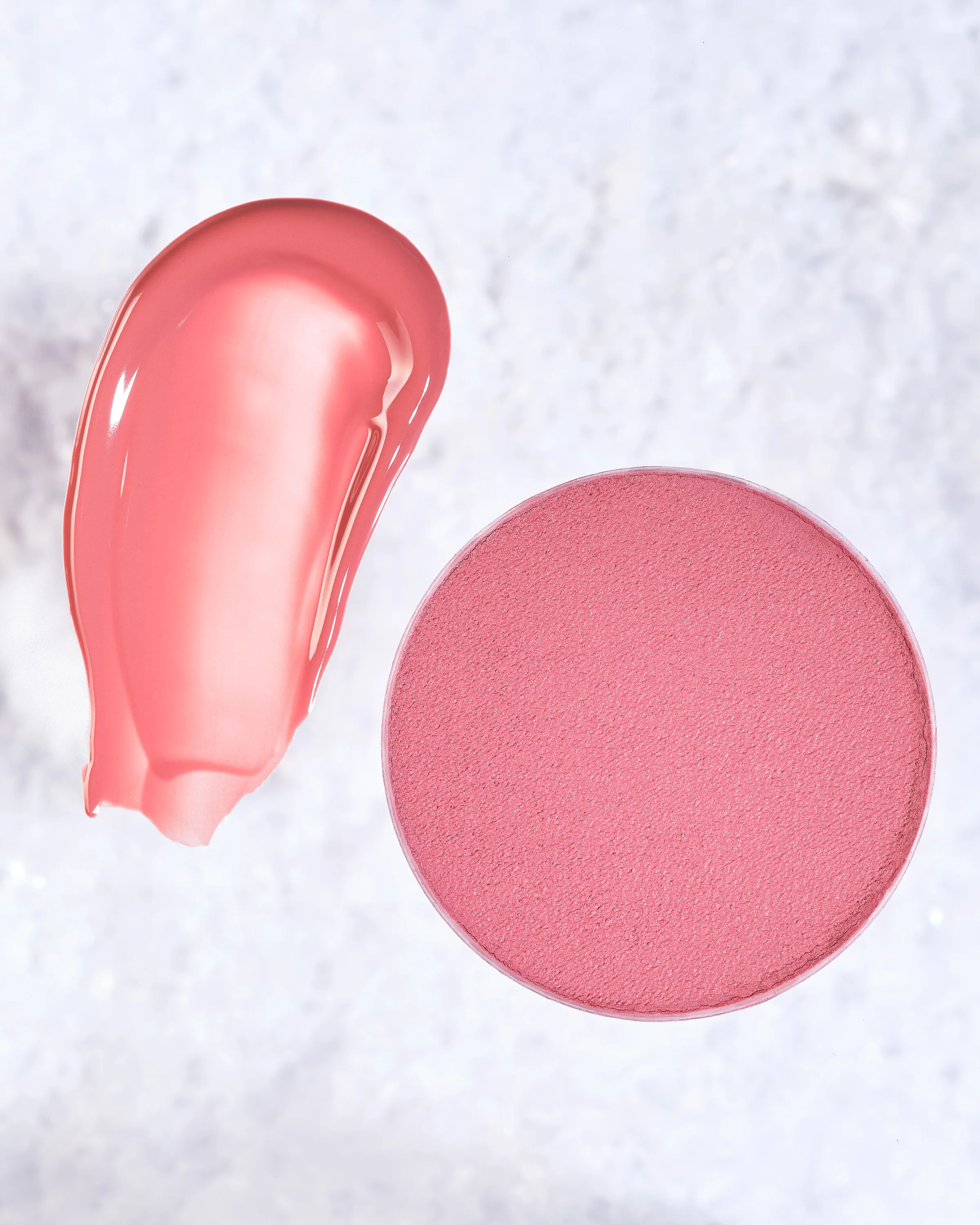 Pink lip gloss smear beside a round pressed blush pan on snowy white texture, for Kylie Cosmetics.