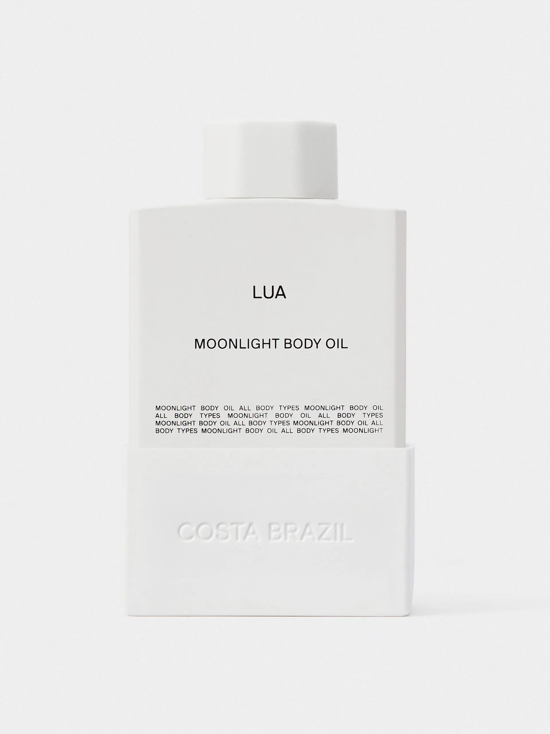 White bottle of Lua Moonlight Body Oil with embossed sleeve on a light grey background, for Costa Brazil.