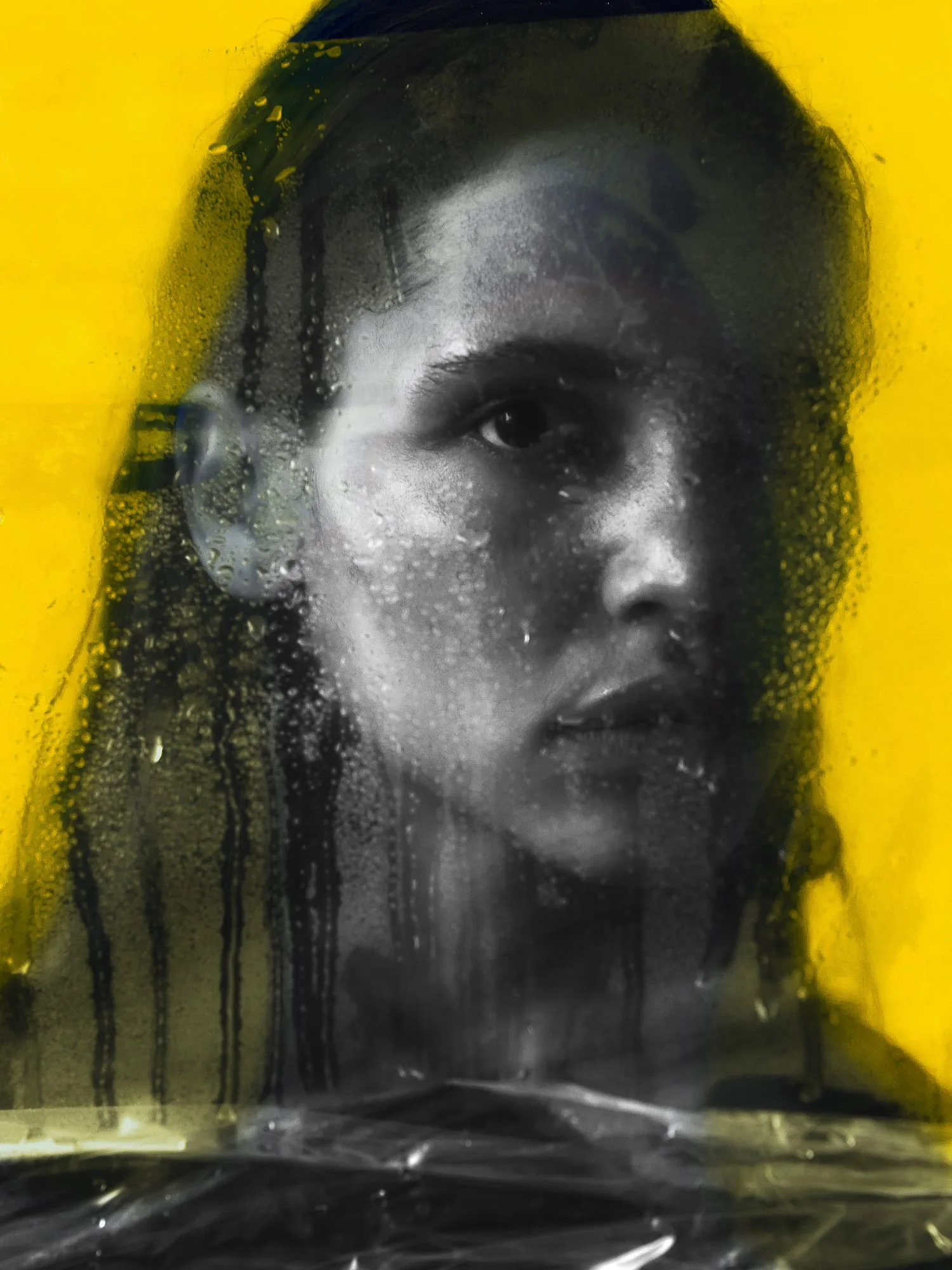 Black and white portrait of a woman behind wet, dripping plastic sheeting against a yellow backdrop, for The Last Magazine.
