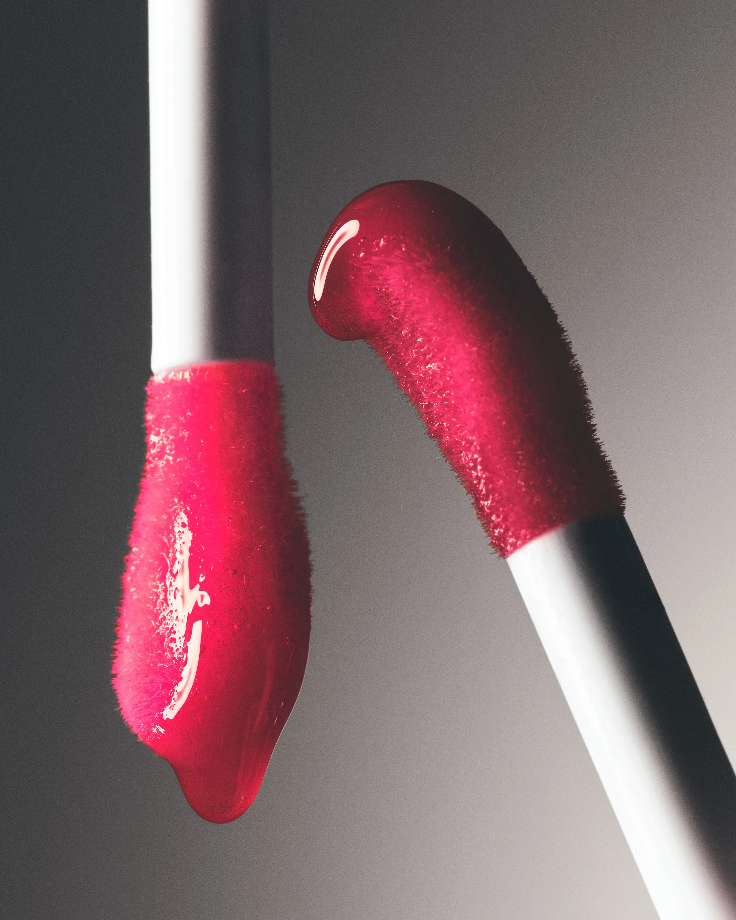Two doe-foot lip applicators dripping glossy red lip product against a grey gradient background, for Kylie Cosmetics.
