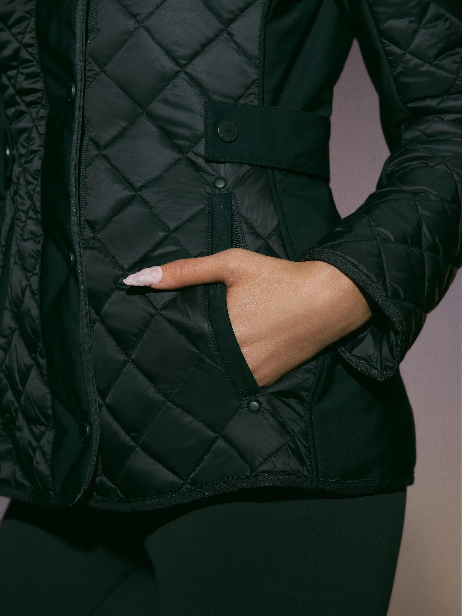 Close-up of a hand in the pocket of a black diamond-quilted jacket with snap tab, for Moose Knuckles.