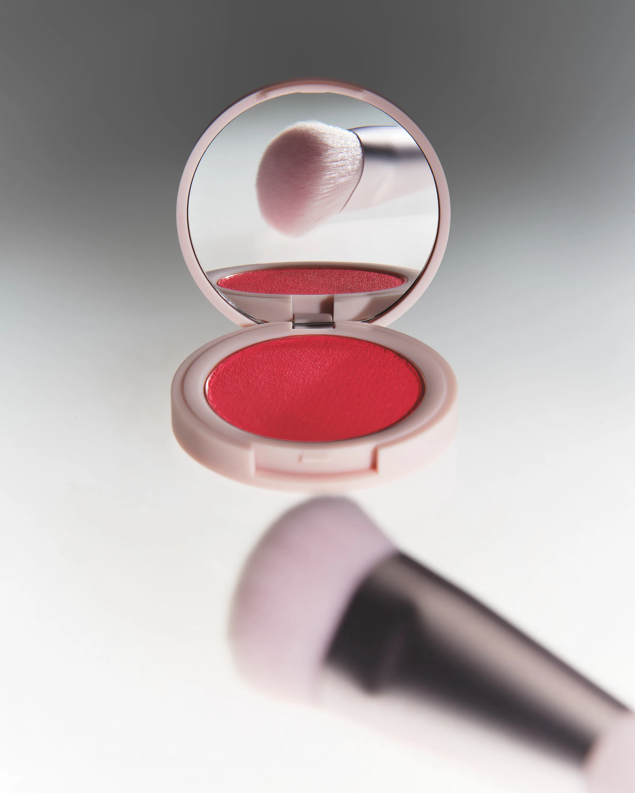 Open pink compact of red Lady Bug hybrid blush with a blush brush reflected in its mirror, for Kylie Cosmetics.