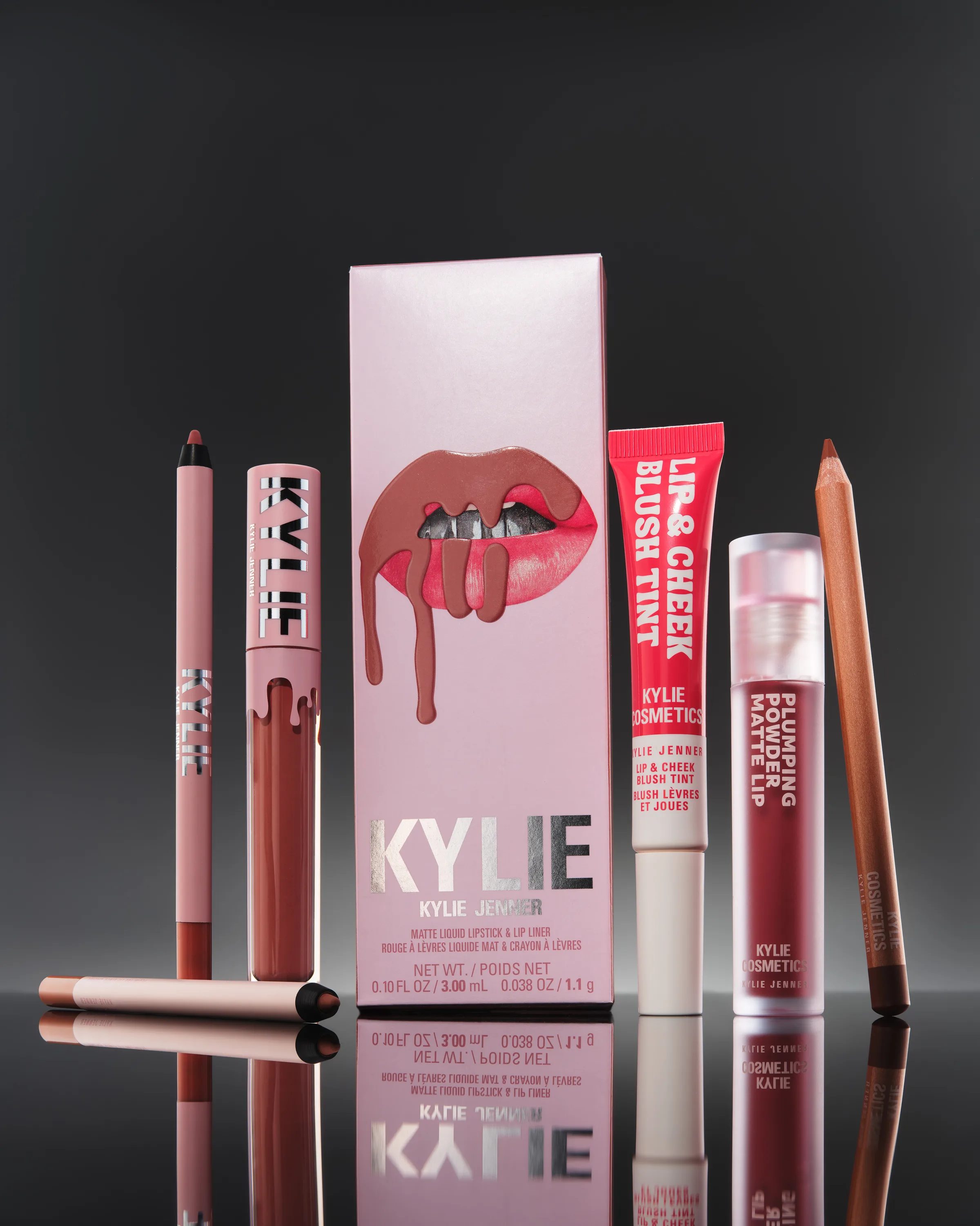 Pink lip kit box with liquid lipstick, lip pencils, blush tint and matte lip on a reflective black surface, for Kylie Cosmetics.