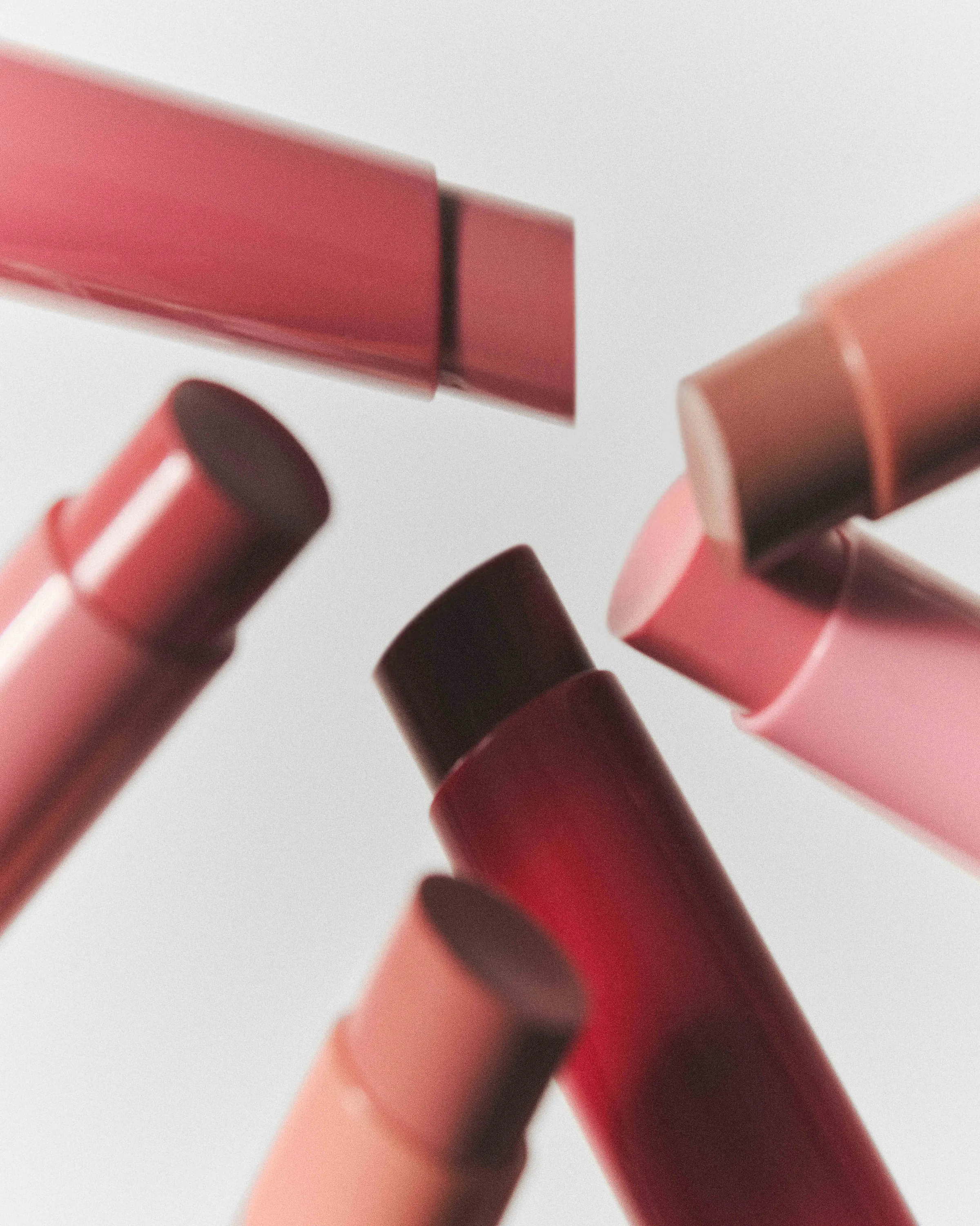 Lip balm sticks in pink, nude and berry shades floating against a pale grey background, for Kylie Cosmetics.