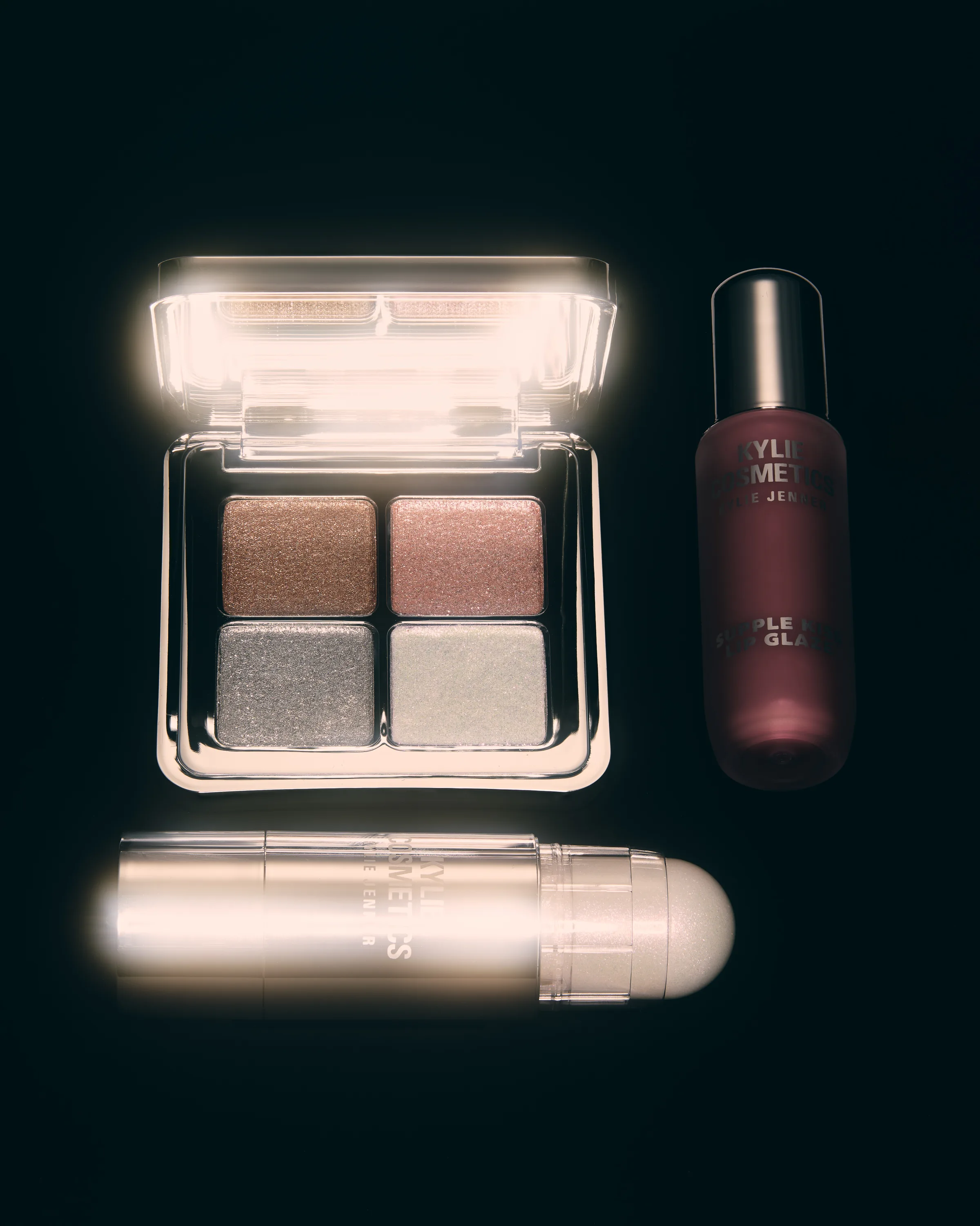 Eyeshadow quad, balm stick and lip glaze glowing with light on a black background, for Kylie Cosmetics.