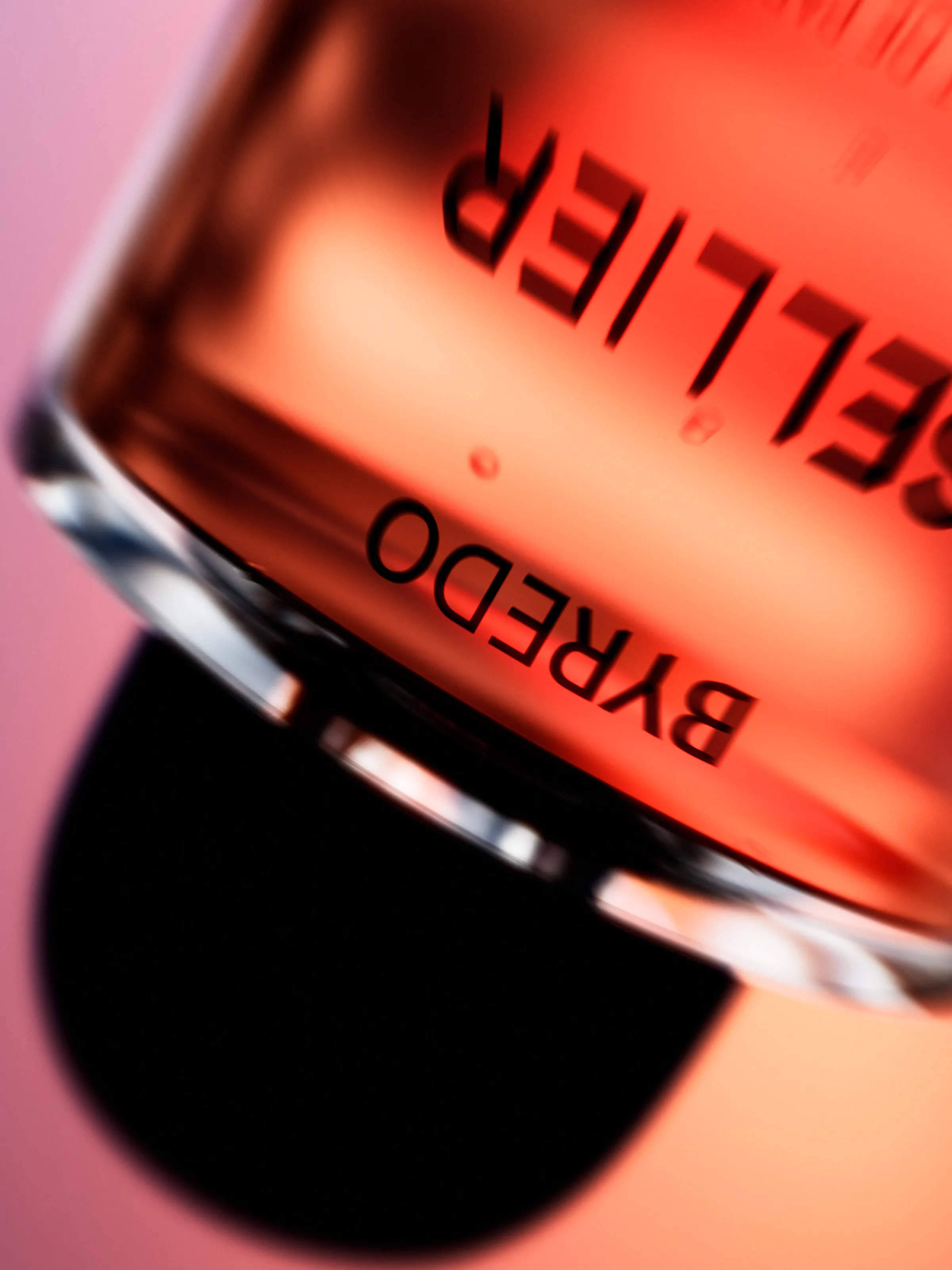 CGI render of an upside-down Byredo perfume bottle with orange liquid and black cap on a pink background, for Byredo.