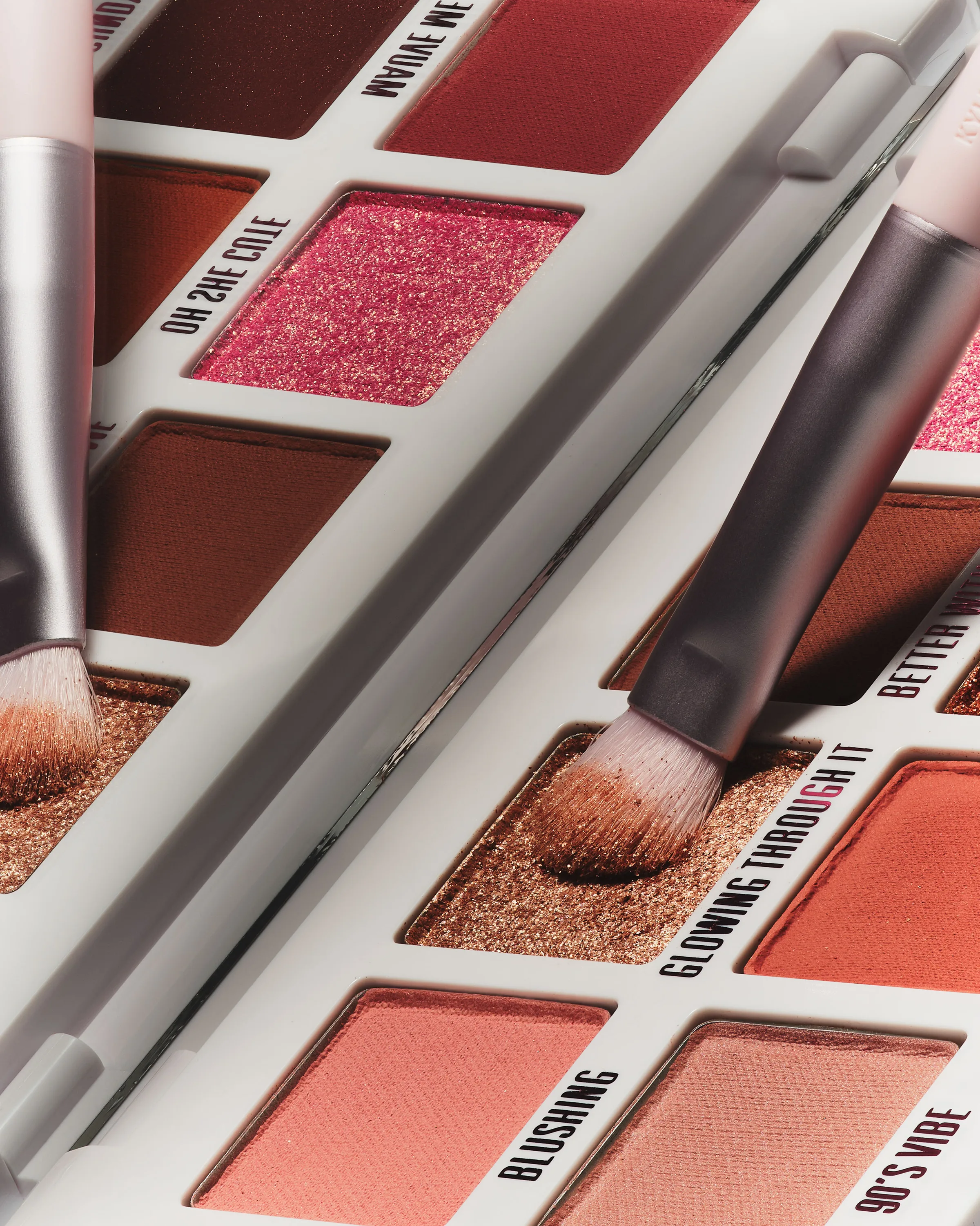 Close-up of a warm-toned eyeshadow palette with brushes dipped in shimmery bronze shade Glowing Through It, for Kylie Cosmetics.