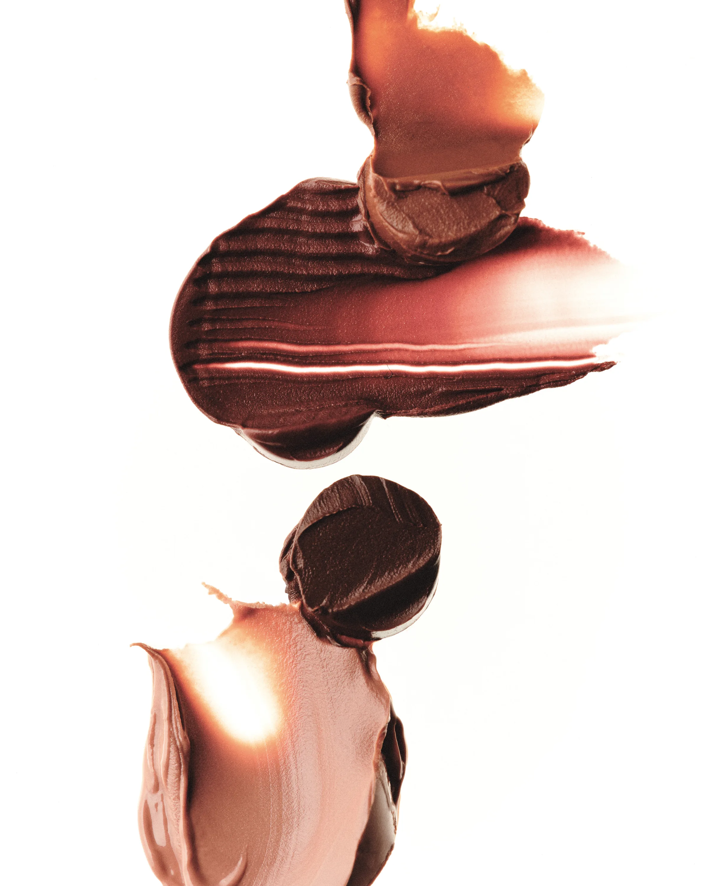 Smeared swatches of brown, bronze and nude cream makeup arranged vertically on a white background, for Kylie Cosmetics.