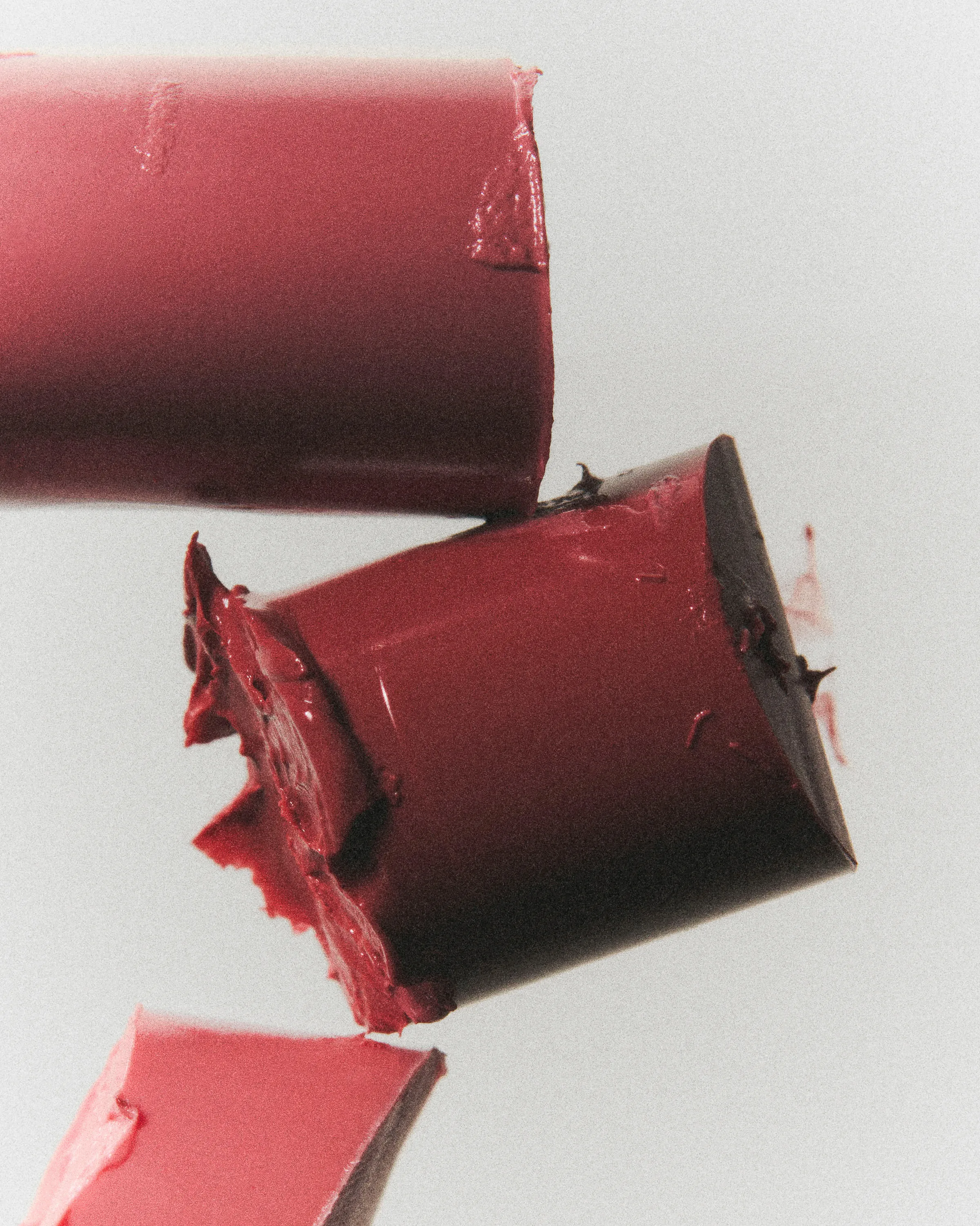 Close-up still life of broken red lipstick pieces with smeared edges against a pale grey backdrop, for Kylie Cosmetics.
