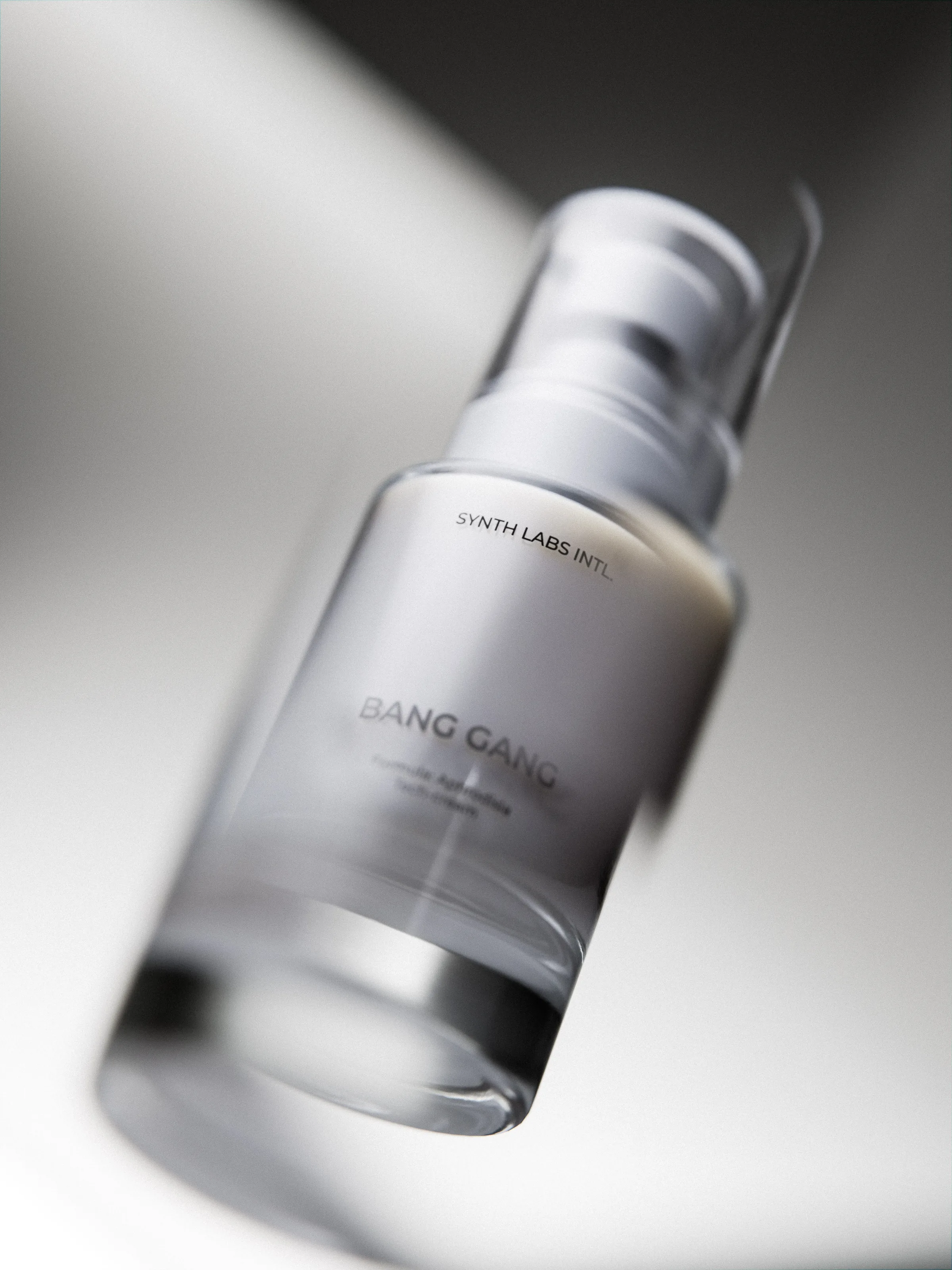 CGI render of a frosted glass serum pump bottle labelled Bang Gang, tilted in soft grey light, for Synth Labs Intl.
