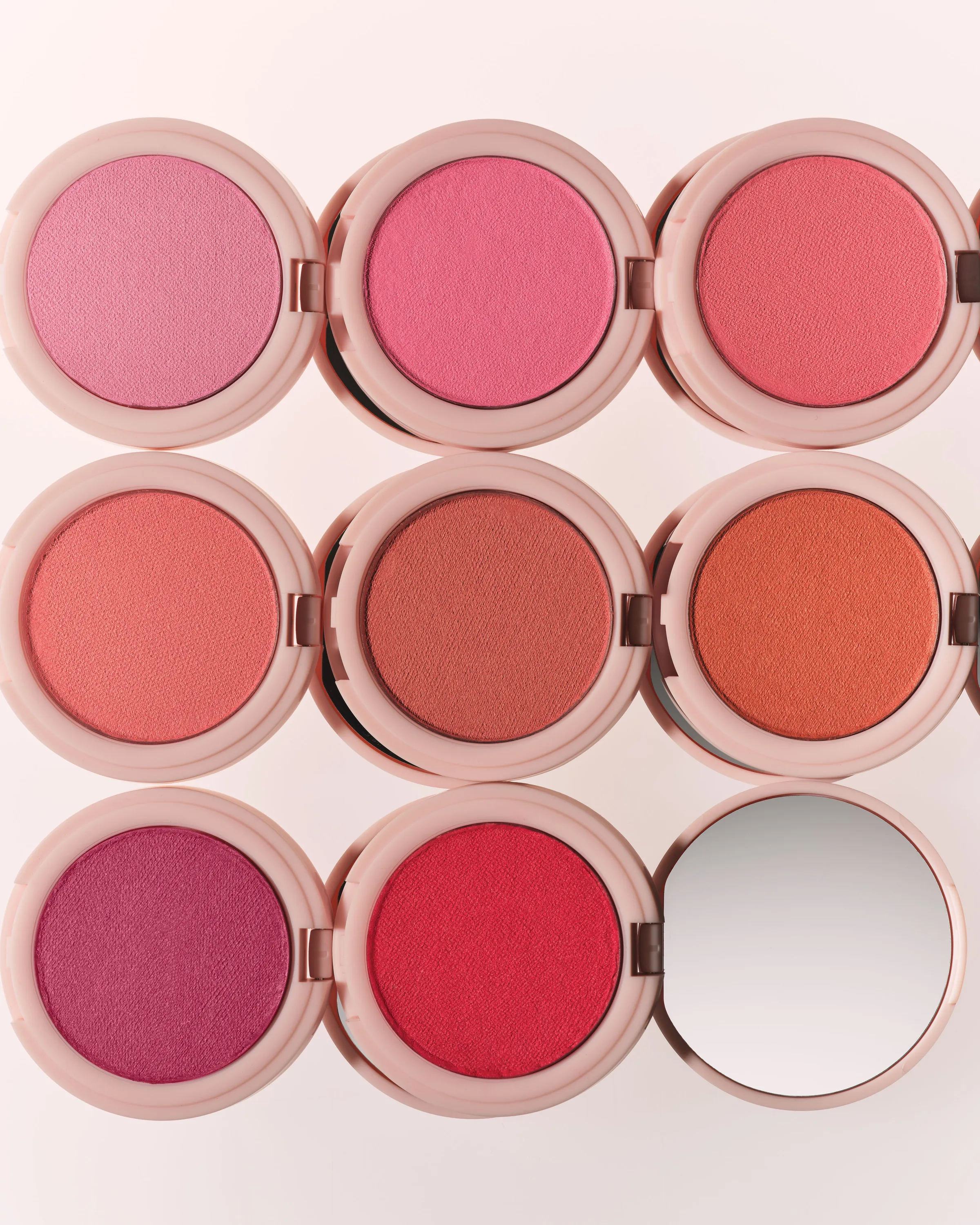Grid of open pink blush compacts in shades from rose to coral and red, one showing its mirror, for Kylie Cosmetics.